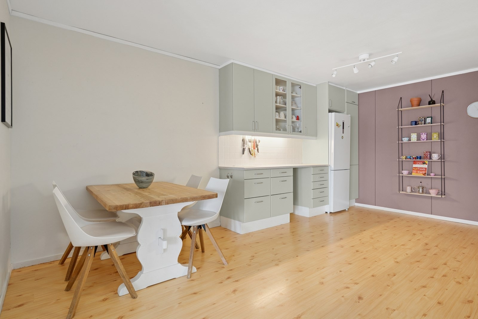 Kjøkkeninnredningen består av malte slette fronter, benkeplate i laminat med nedfelt kjøkkenvask og fliser på vegg over benk. Galleribilde