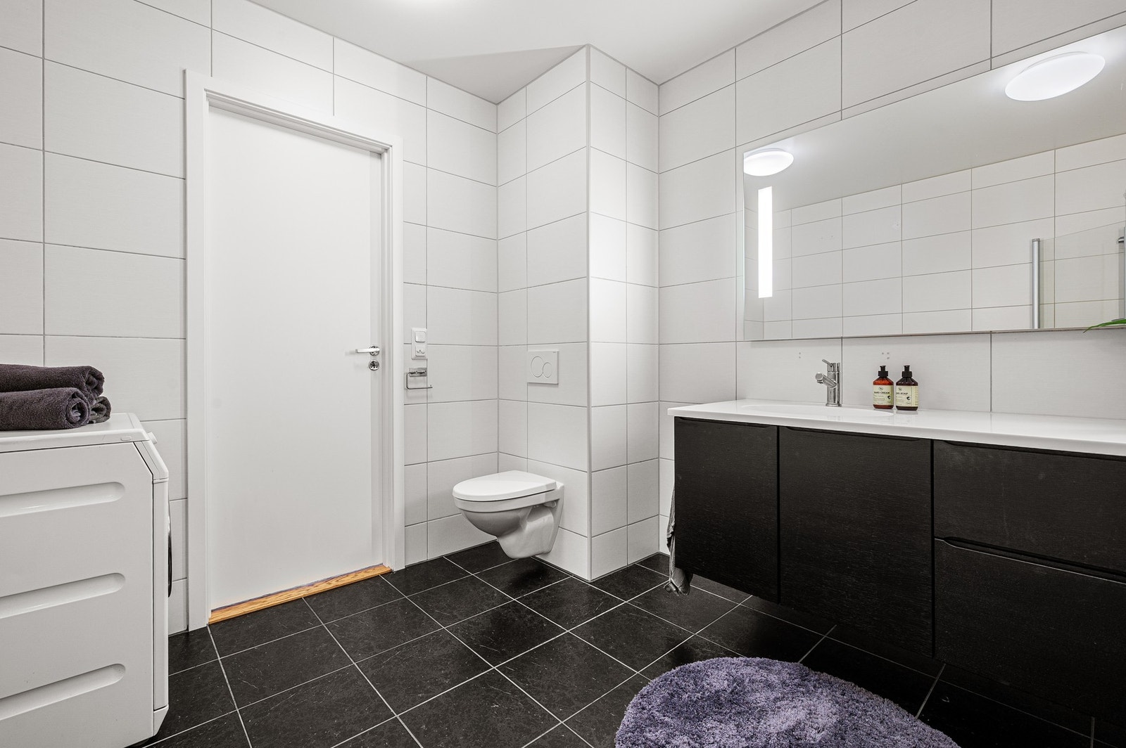 Badet er utstyrt med varmekabler i gulv, dusjhjørne, vegghengt toalett, vegghengt innredning med god oppbevaringsplass samt belyst speil. Galleribilde