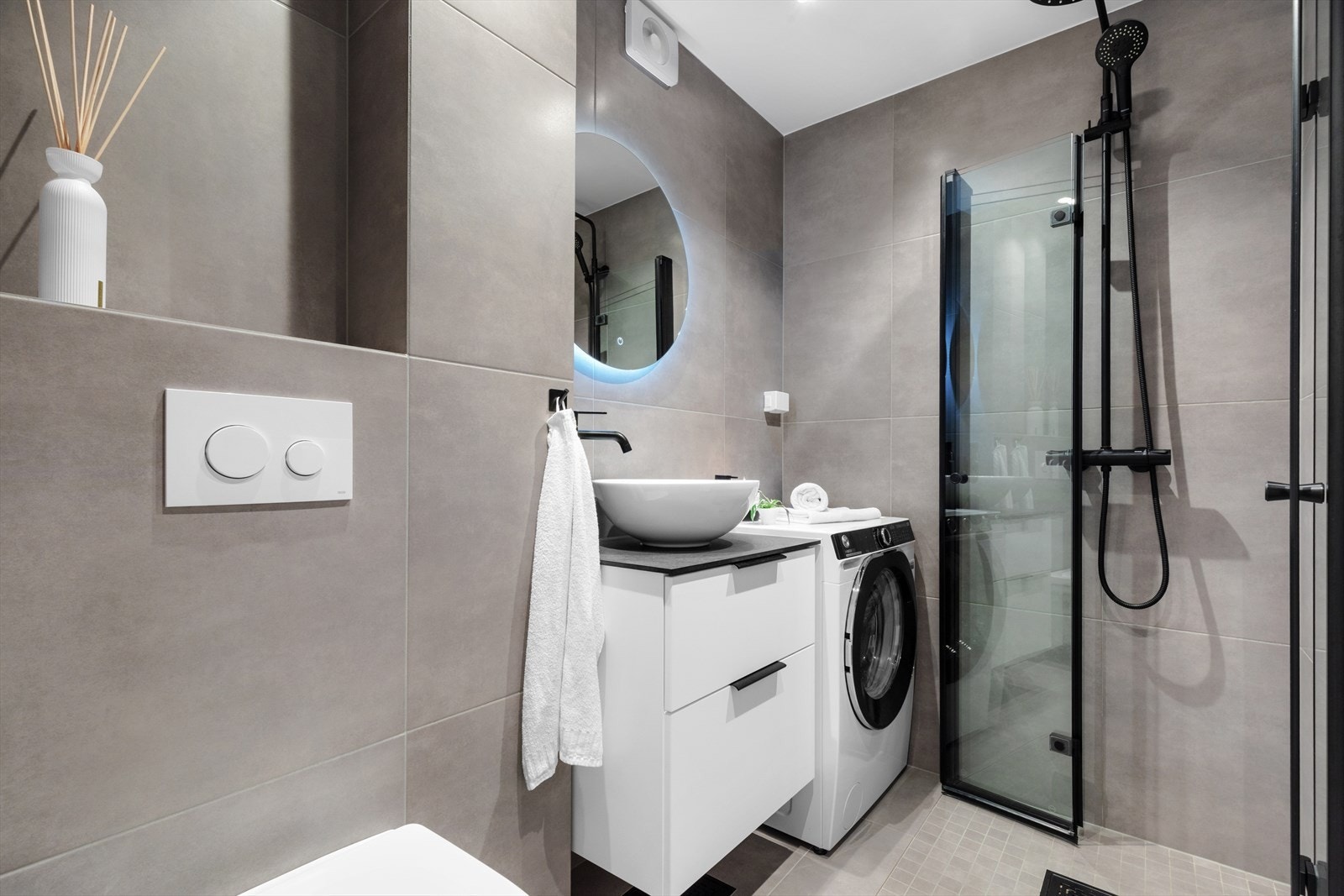 Varmekabler og downlights er installert, og badet har vegghengt toalett og et dusjhjørne med stilig glassvegg i sort innramming og mosaikkfliser. Galleribilde