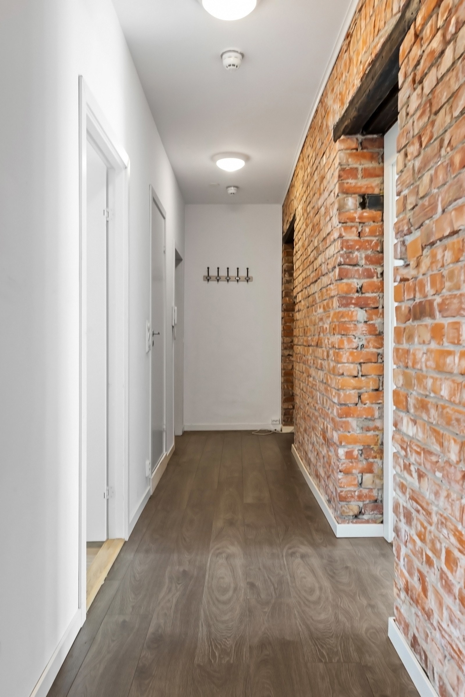 Entréen er lys og innbydende med nyere, brannkvalifisert entrédør, mørkt laminatgulv i enstavs design fra 2019, lysmalte vegger, glatt, hvitmalt himling og hvite, glatte innerdører. Det er knagger på veggen og plass til skohylle eller lignende i rommet. Galleribilde