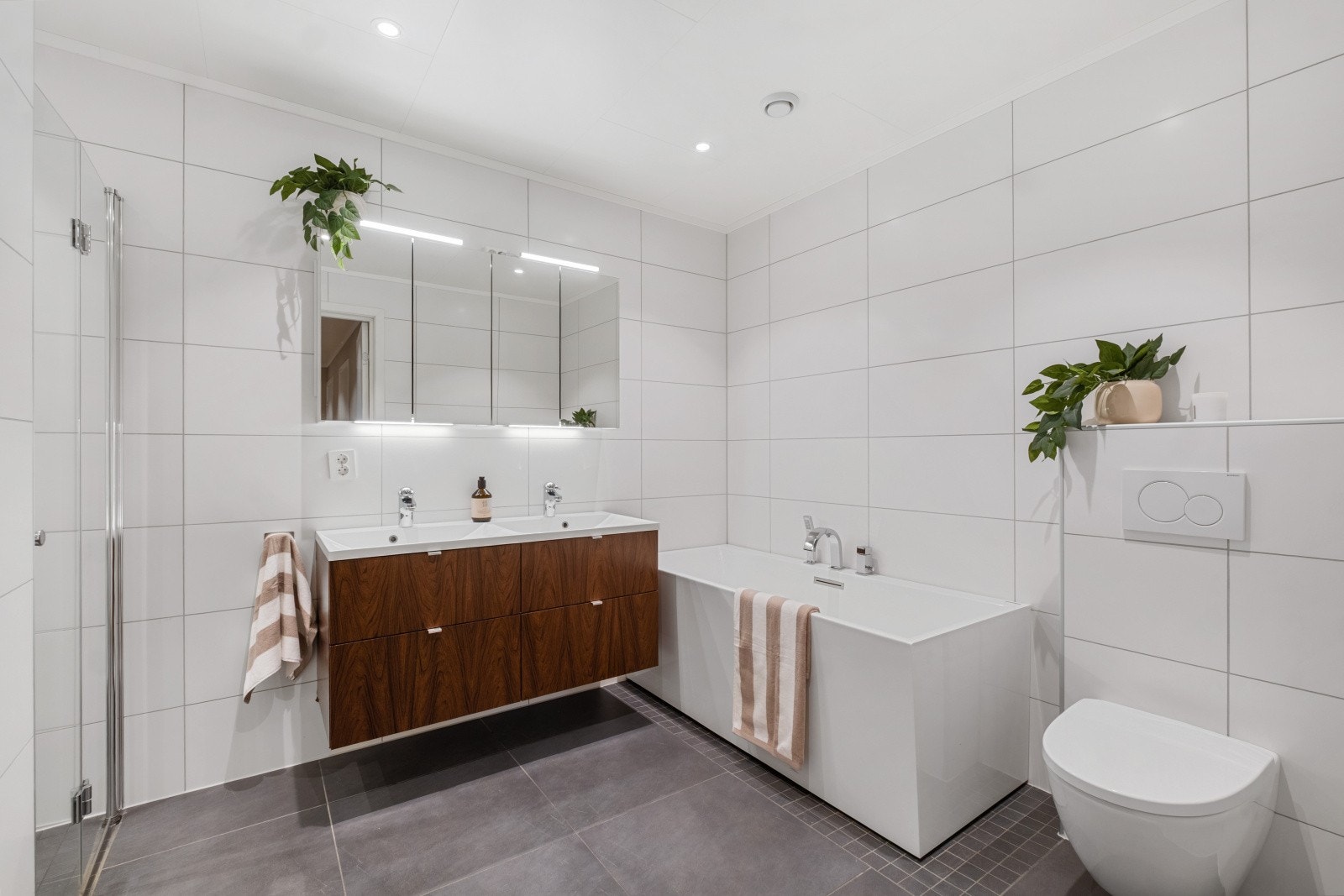 Badet er stilrent med store mørke gulvfliser og hvite avlange veggfliser Galleribilde