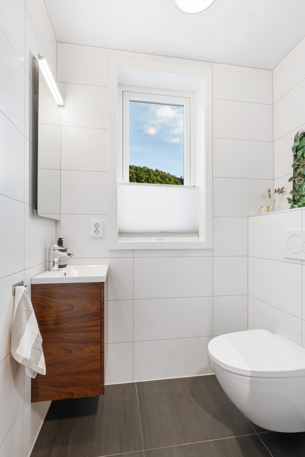 Toalettrommet har flislagte overflater i nøytrale farger - Her er det vegghengt toalett og servantinnredning med speil over Galleribilde