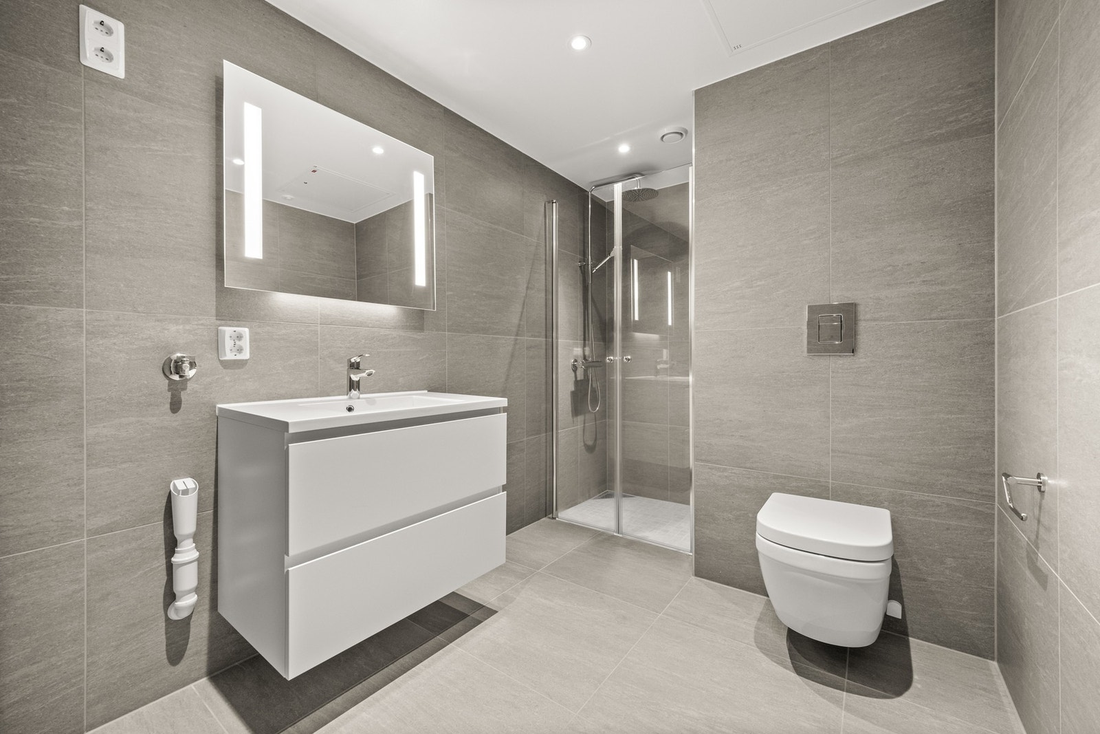 Det flislagte badet har downlights i tak, vannbåren gulvvarme og opplegg for vaskemaskin og tørketrommel Galleribilde