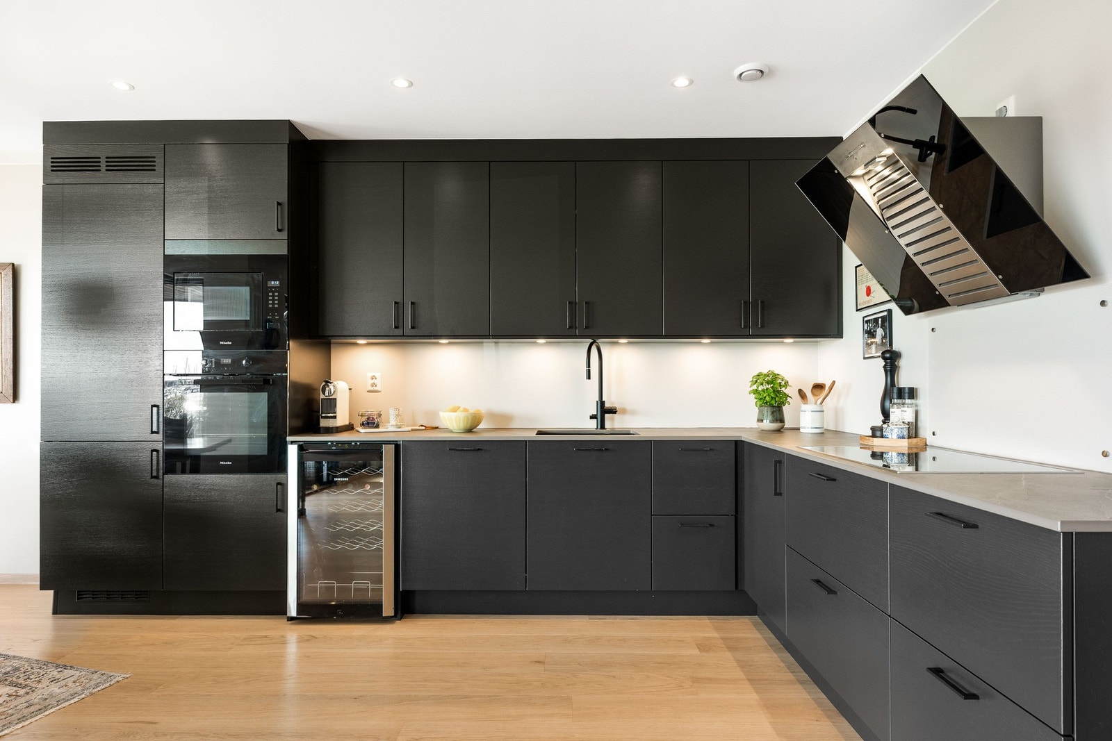 Romslig og moderne takhøyt kjøkken fra Strai i åpen løsning med mørke skapfronter, lys benkeplate, integrerte hvitevarer og stilrent design. Galleribilde