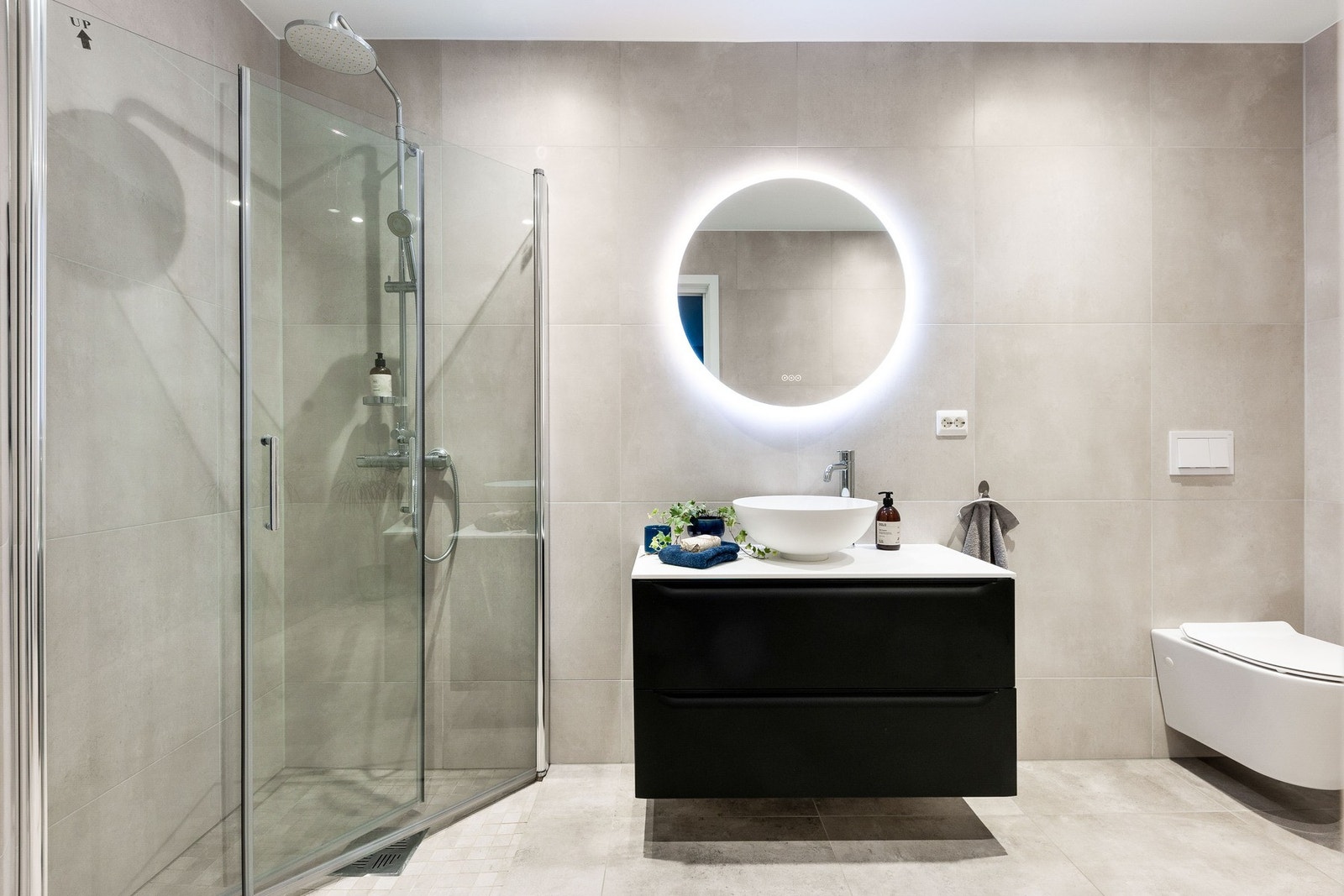 Moderne og delikat bad med mørk baderomsinnredning, dusjkabinett og vegghengt toalett. Lyse og tidsriktige fliser gir et godt førsteinntrykk til badet. Galleribilde