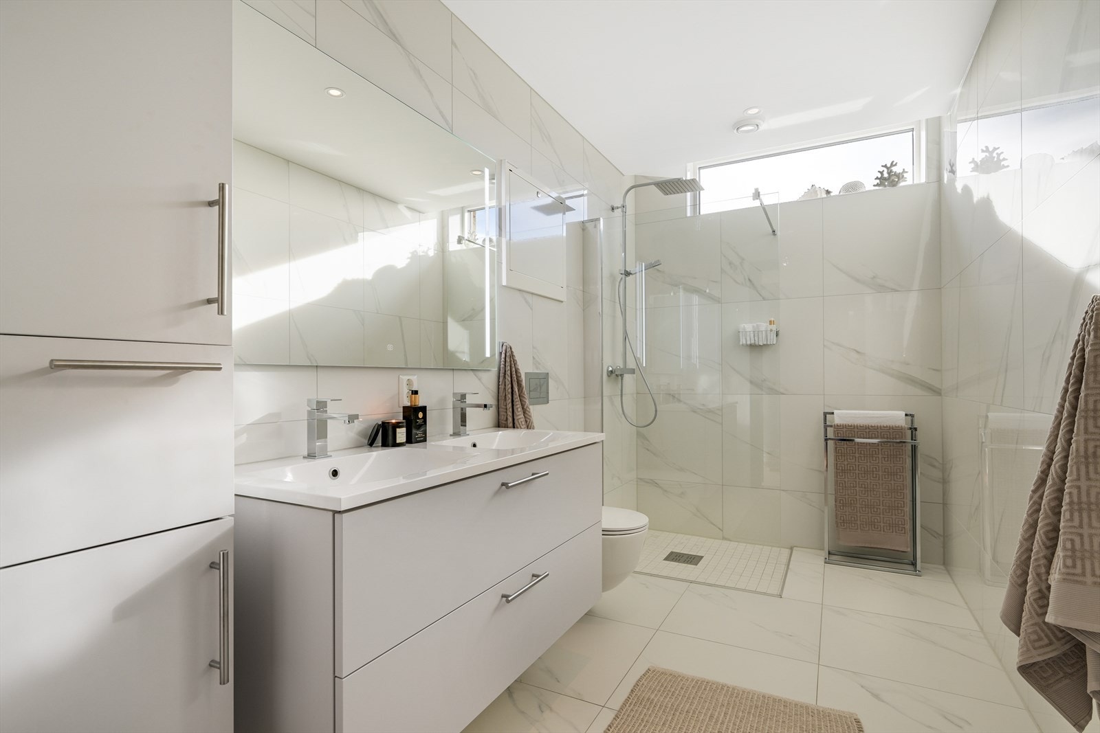 Leiligheten sitt andre baderom er særdeles stort og fullverdig, samt helfliset på gulv og vegger. Rommet er påkostet med baderomsinnredning med dobbel heldekkende servant og skuffeseksjon, tilhørende høyskap og belyst speil montert på vegg. Galleribilde