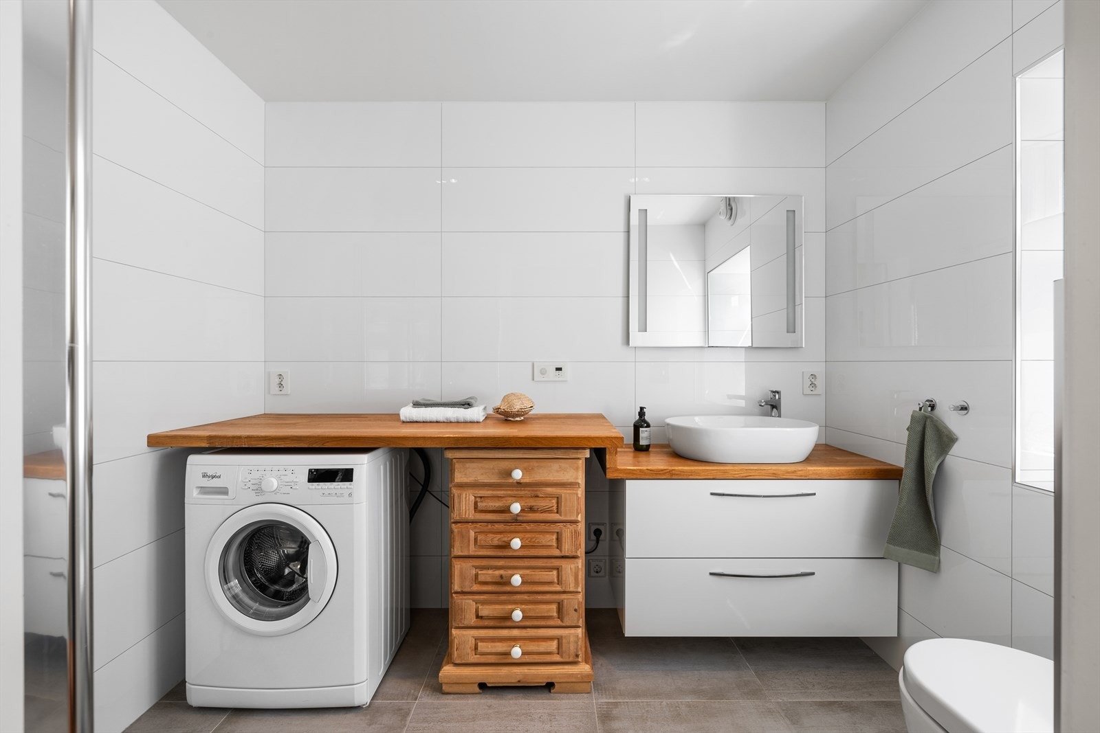 Det er også speil med integrert belysning, servantseksjon med oval bolleservant og veggmontert toalett med hylle over skjult sisterne. I tillegg er det opplegg for vaskemaskin og tørketrommel. Galleribilde