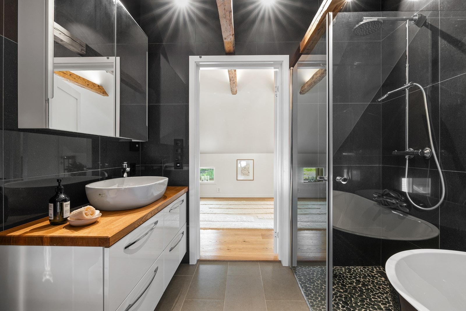 Badet i andre etasje har i tillegg et stilig badekar for ekstra velvære. Rommene har fliser og rullestein på gulvene, samt store, høyglanspolerte fliser på veggene. Synlige trebjelker i himlingen matcher servantinnredningens benkeplate. Galleribilde