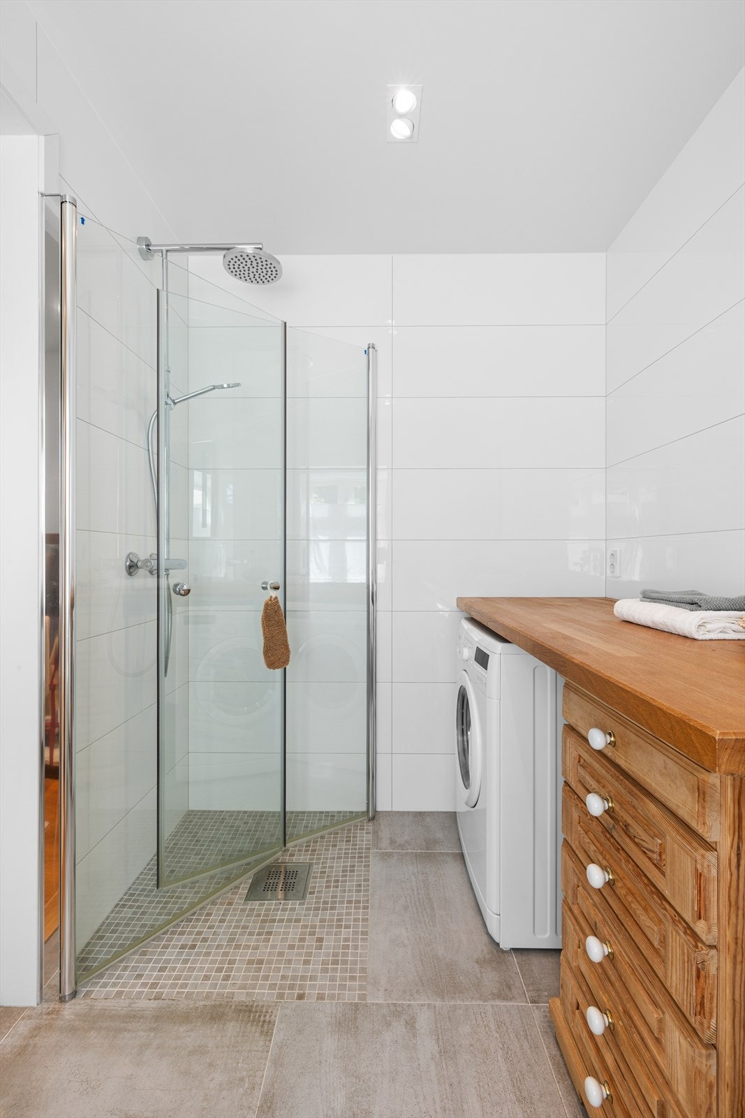 Badet i første etasje fremstår som delikat med flotte oppbevaringsløsninger og et vindu med hyggelig utsyn og dyp vinduspost. Rommet har store, sjatterende fliser på gulvet og lyse fliser på veggene. Galleribilde