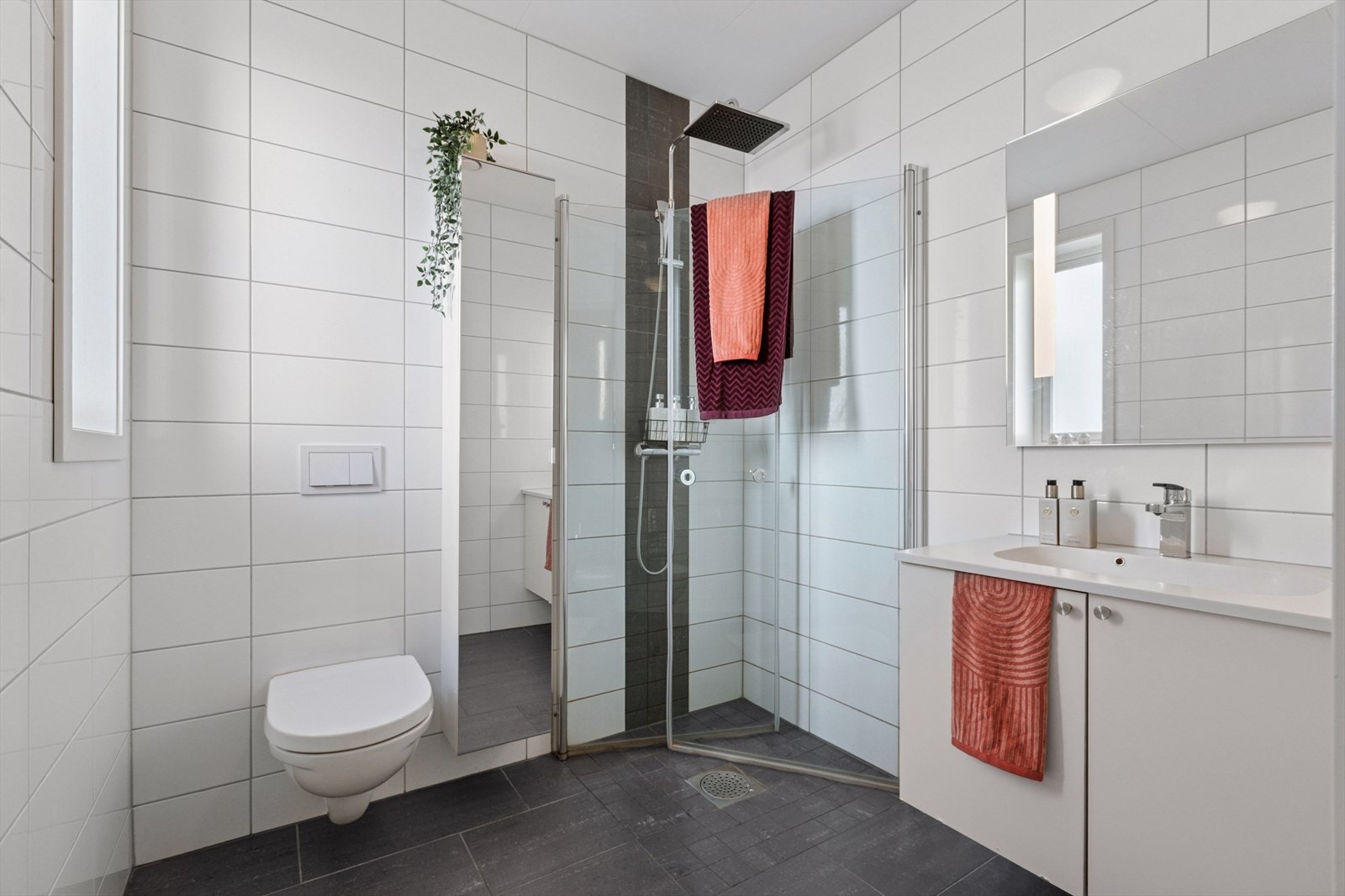 Flislagt bad på 4 m² utstyrt med blant annet gulvvarme, vegghengt klosett, innfellbare dusjvegger og servant med oppbevaringsplass. Galleribilde