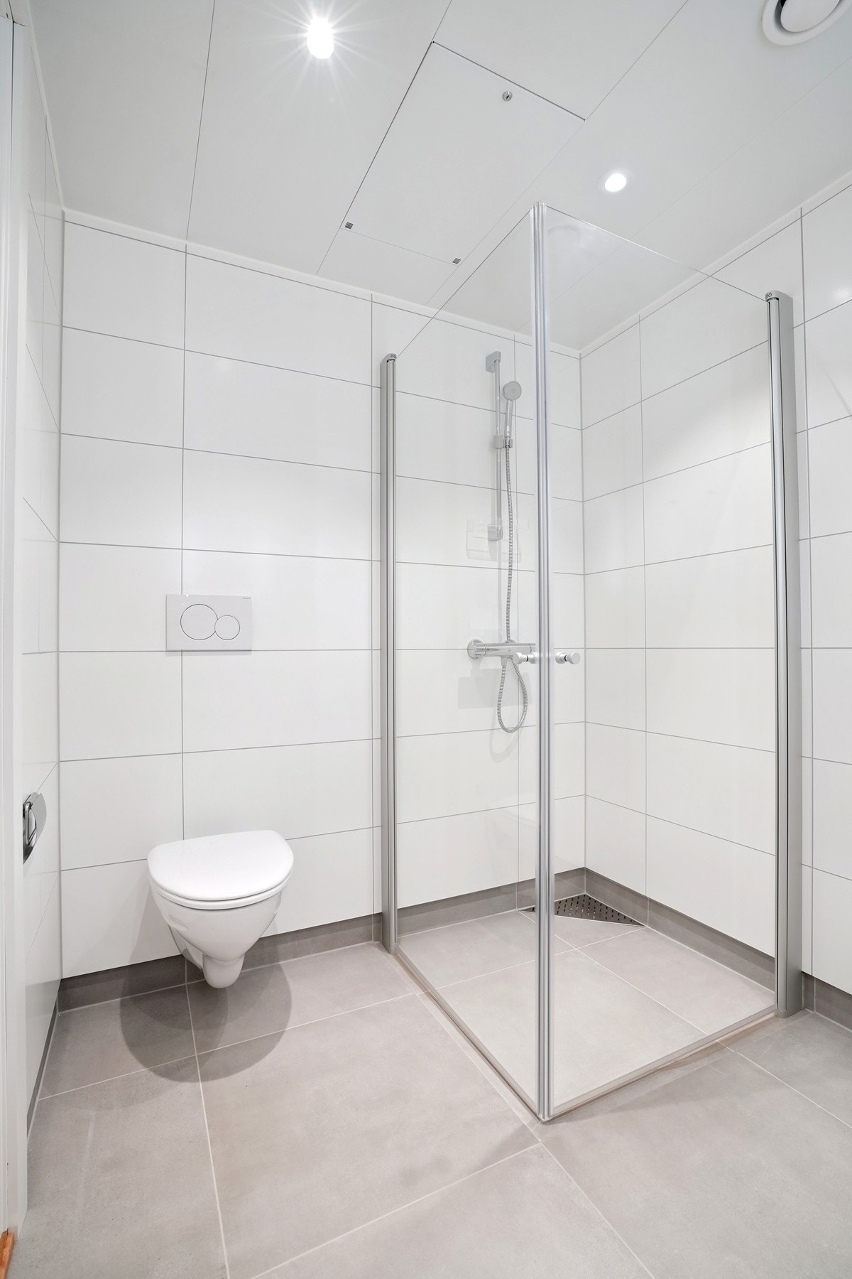 Praktiske dusjdører i glass. Downlights i tak og vegghengt toalett gir en moderne og funksjonell helhet. Galleribilde