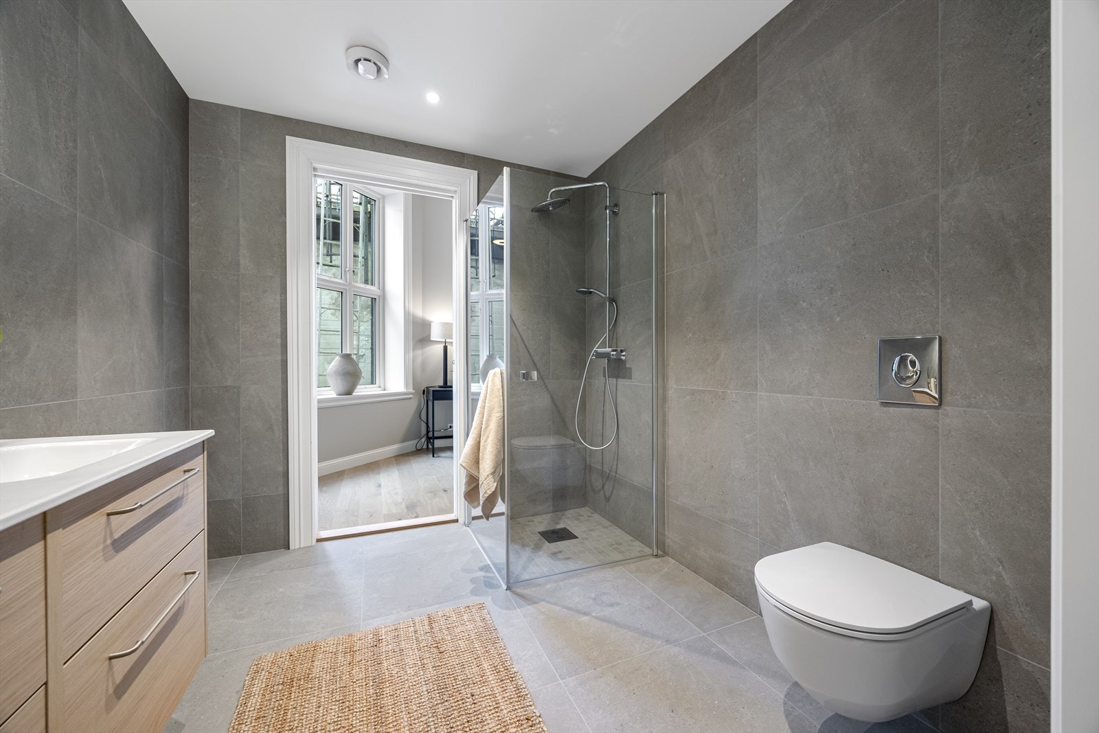 Leiligheten har 2 komplette bad, begge med fliser til tak (store 60 x 60 fliser) i grå utførelse, dusjhjørner med glassvegg og mosaikk på gulv. Galleribilde