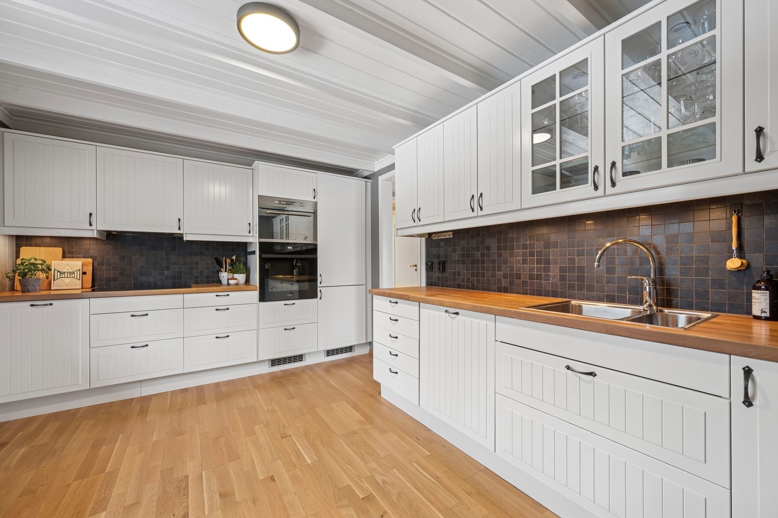 Kjøkkeninnredning med hvite profilerte fronter og benkeplate av tre med fliser på vegg over benkeplaten. Galleribilde