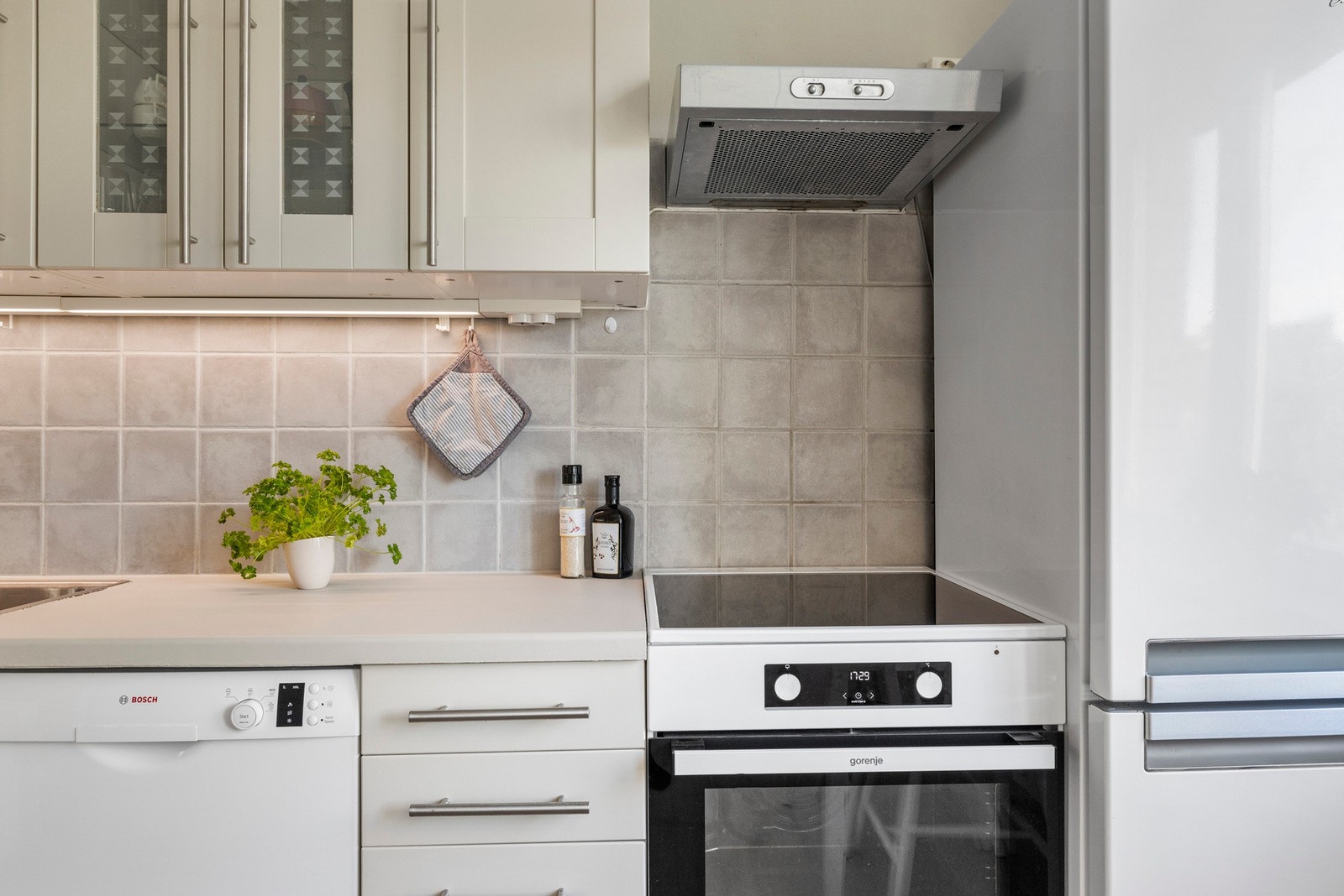 Innredning med profilerte fronter, laminert benkeplate med nedsenket oppvaskkum og ett-greps armatur, frittstående komfyr med keramisk platetopp, frittstående kjøleskap med frysedeø og separat fryseboks, frittstående oppvaskmaskin og ventilator med belysn Galleribilde