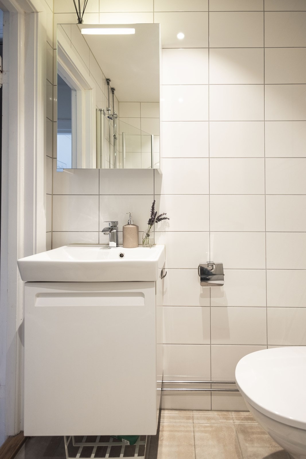 Badet er innredet med vegghengt toalett, servant med innredning, speilskap med lys og dusjhjørne med svingbare glassdører. Galleribilde