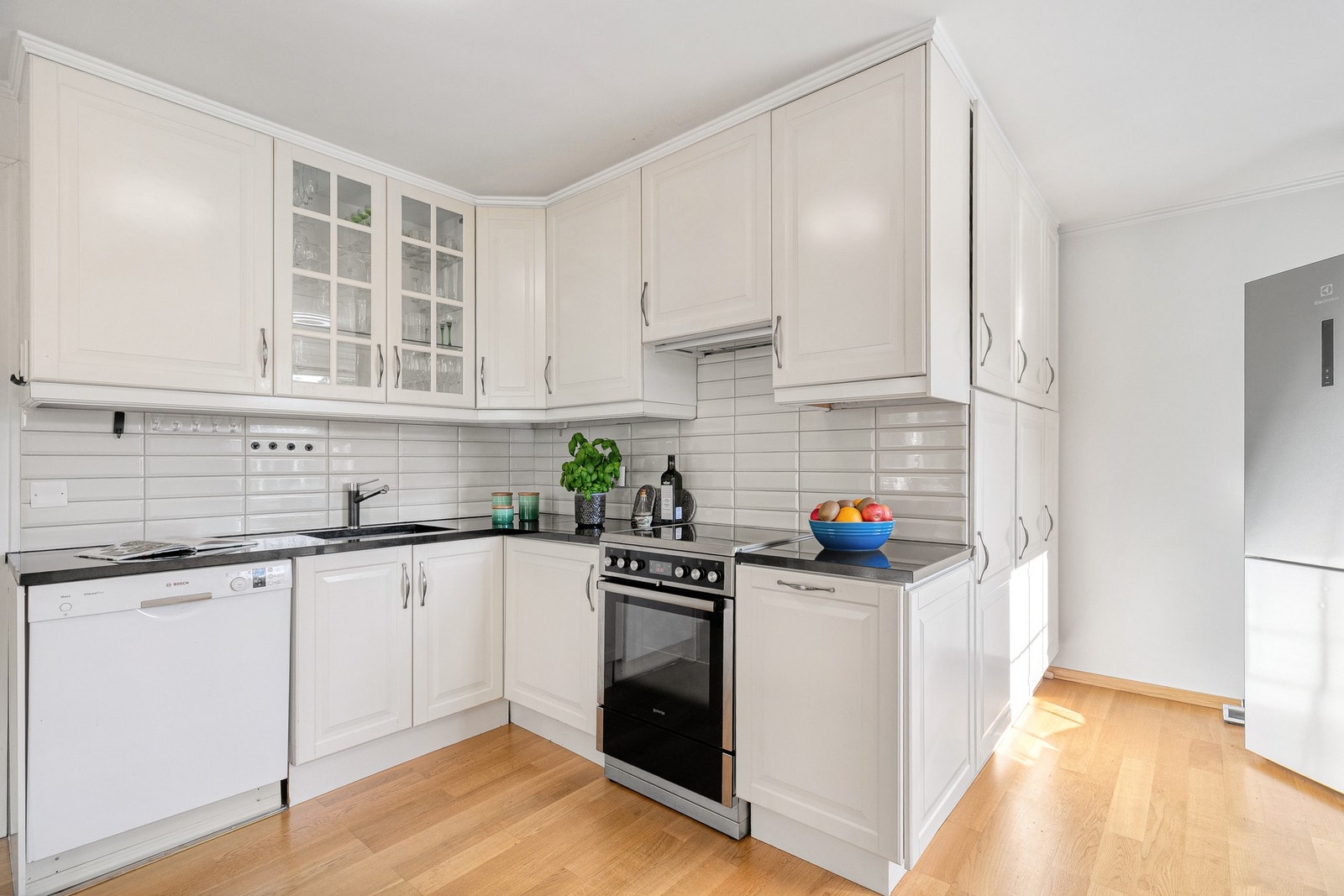 Pent kjøkken med hvitevarer og vitrineskap. Galleribilde