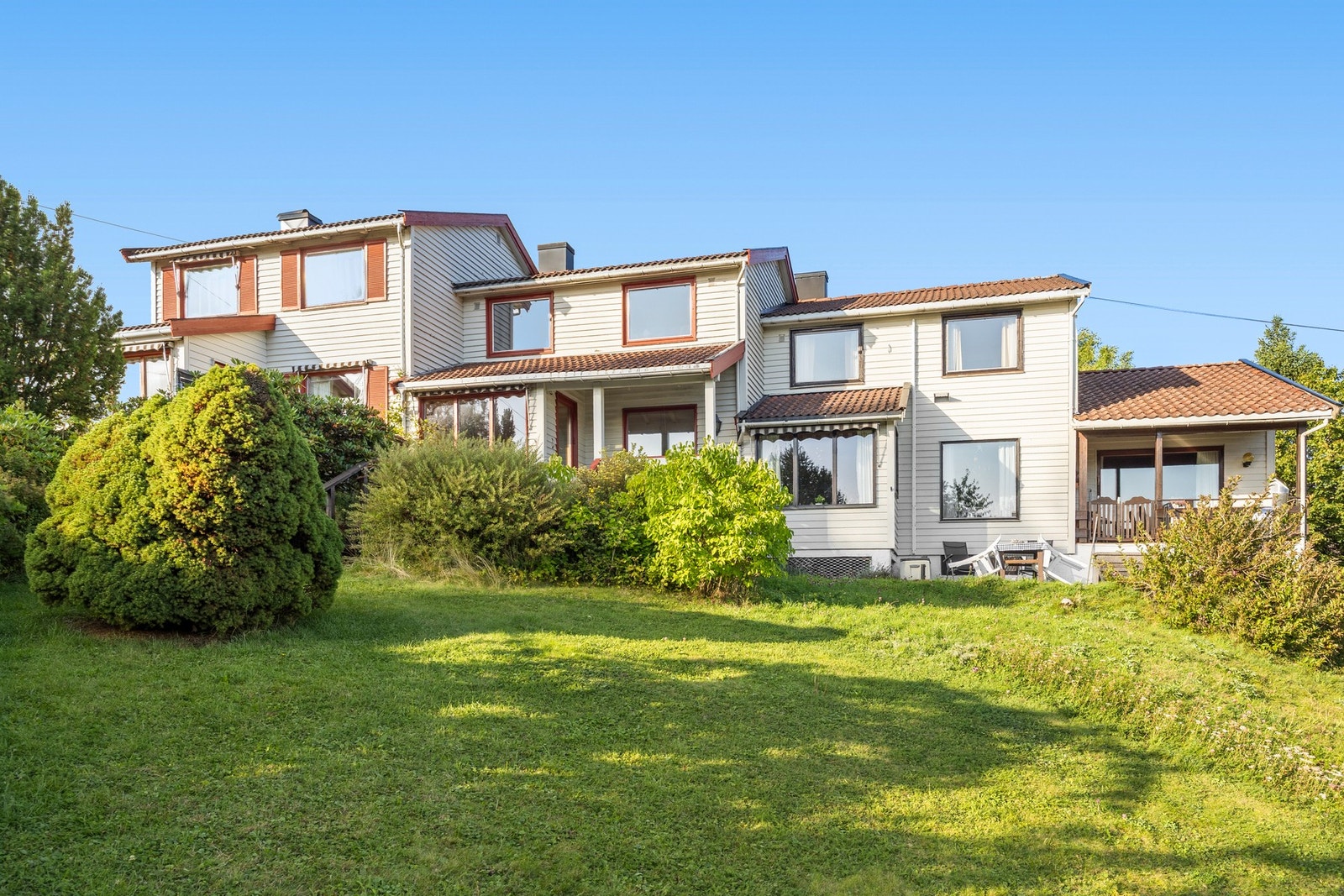 Uteområdet vender mot sørvest og har hage som er innrammet av prydbusker og trær Galleribilde