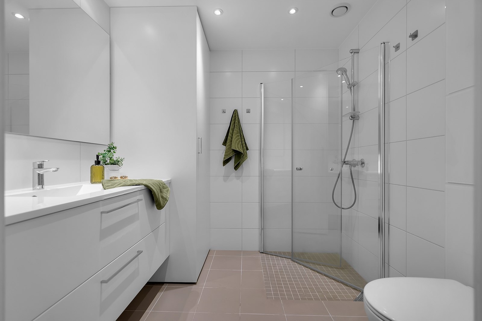 Baderommet er lekkert helfliset og innredet med dusjnisje som har plassbesparende glassvegger, servant med underskuffer og vegghengte toalettet. Opplegg til vaskemaskin, diskret plassert i et integrert baderomsskap som holder rommet ryddig og organisert. Galleribilde