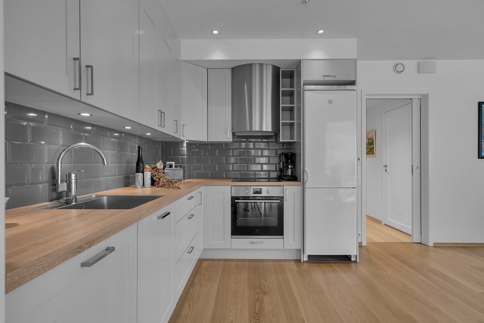 Flotte detaljer som fliser over benkeplaten gir kjøkkenet et elegant preg, mens integrerte hvitevarer som platetopp, stekeovn og oppvaskmaskin sørger for en sømløs og moderne løsning. Galleribilde