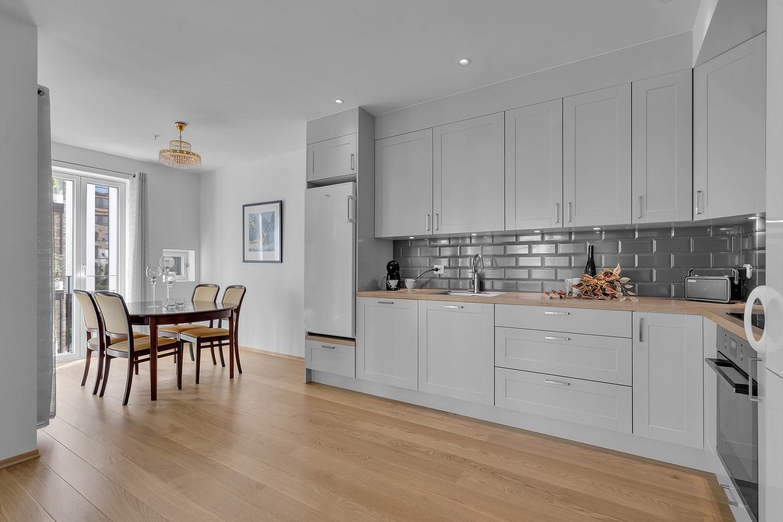 Den åpne løsningen mellom stue og kjøkken skaper en sømløs flyt mellom rommene, perfekt for både hverdag og sosiale sammenkomster. Galleribilde