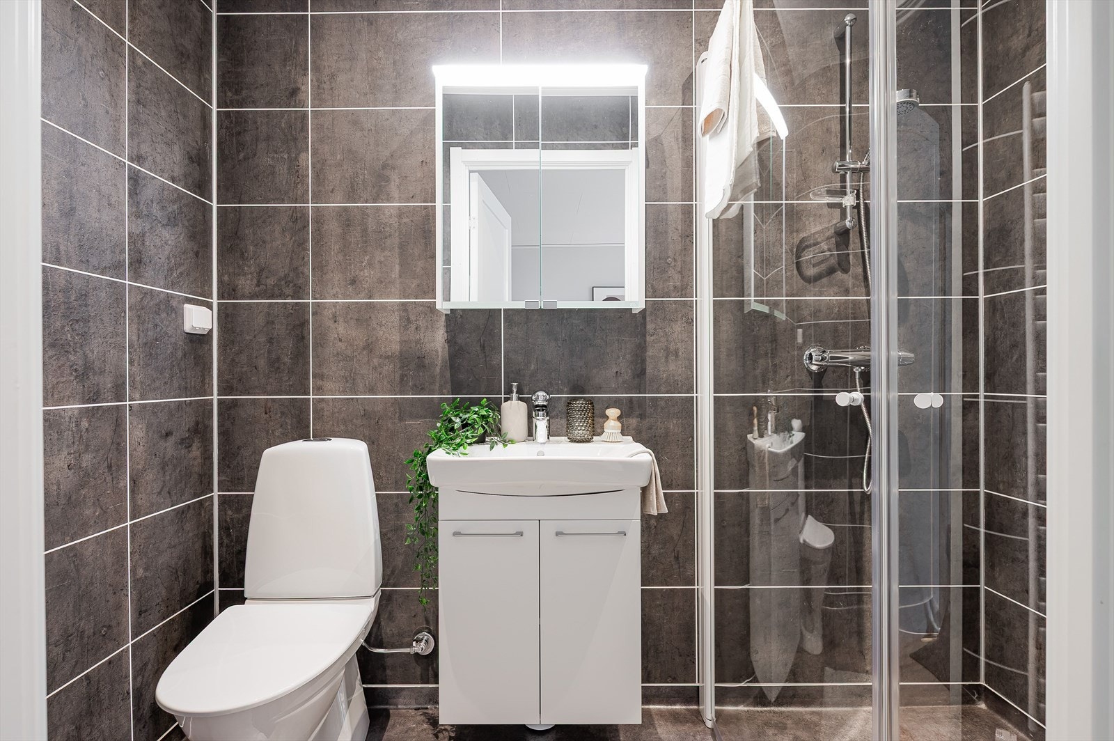 Baderommet tilknyttet soverom 1 er innredet med toalett, servant på innredning og dusjhjørne. Overskap med speil og belysning. Galleribilde