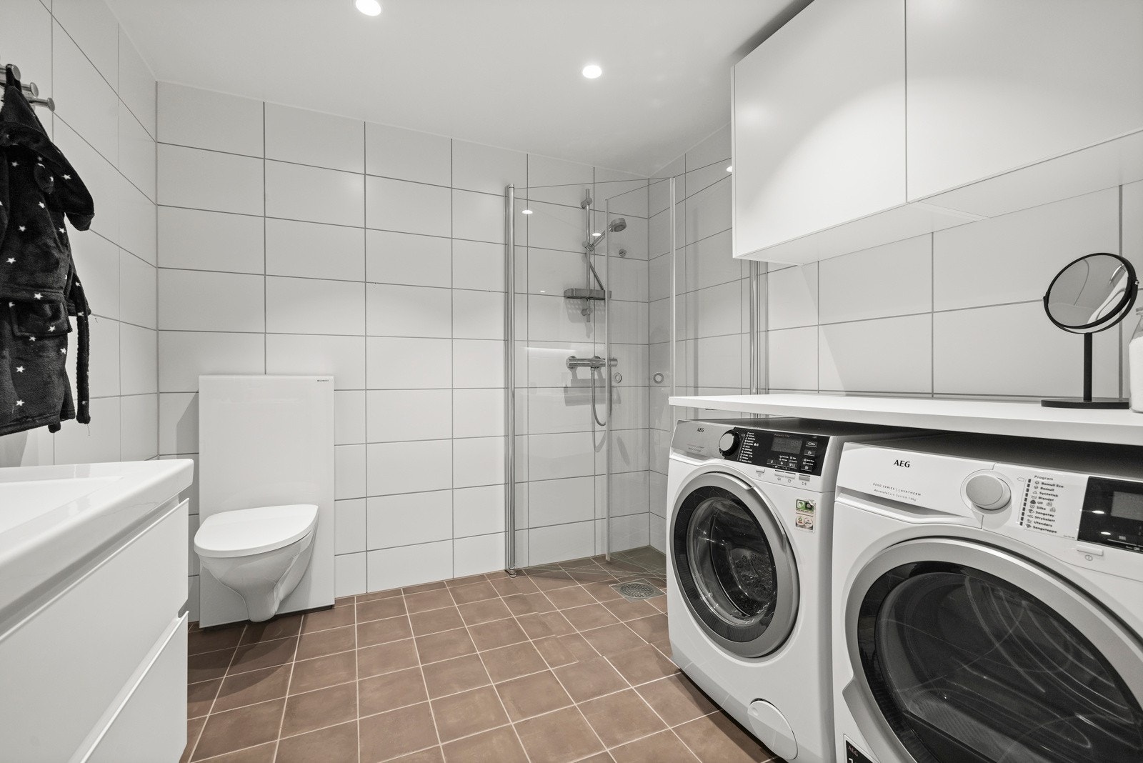 Bad med vegghengt toalett og dusjdører i herdet glass. Opplegg for vaskemaskin og tørketrommel. Galleribilde