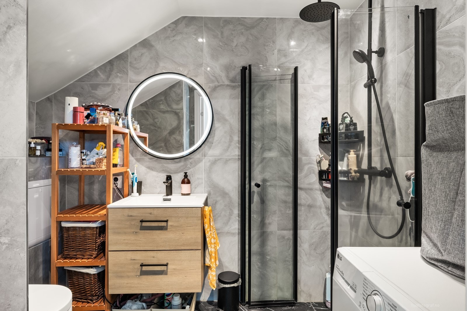 Badet er innredet med vegghengt toalett, dusjhjørne og servant med underskuffer. Over servanten er det montert et rundt speil med integrert belysning. Galleribilde