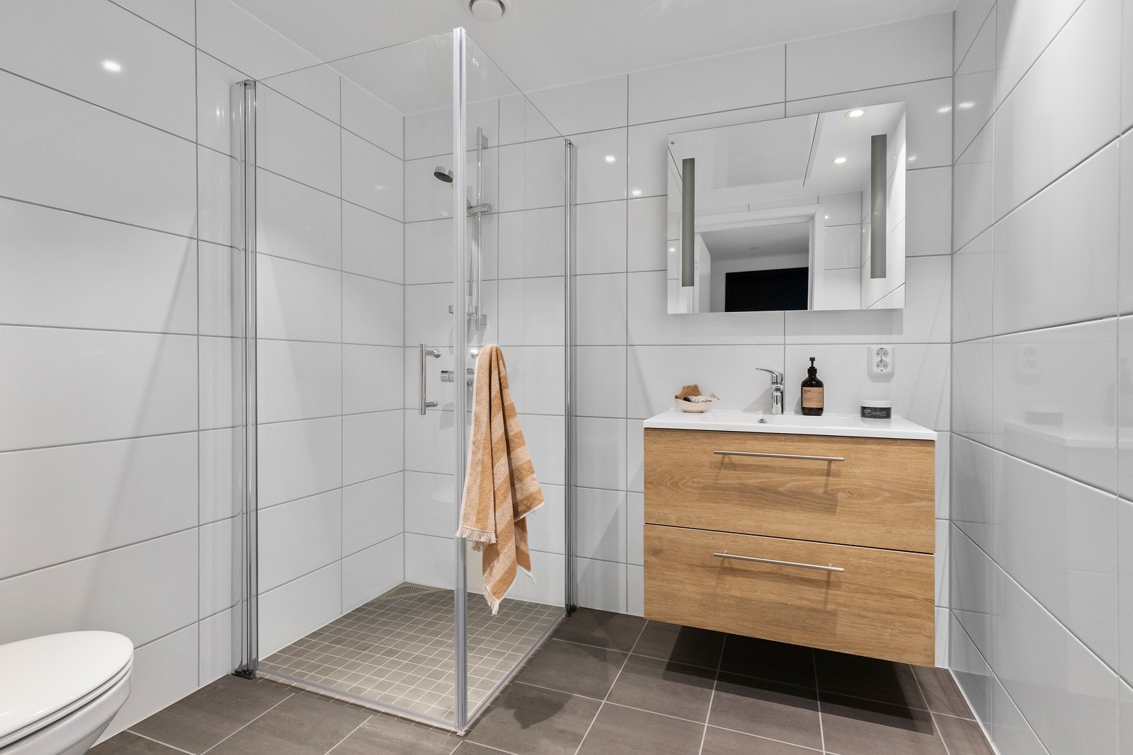 Flislagt baderom med innfellbare dusjvegger, vegghengt toalett og servant med underskap. Galleribilde