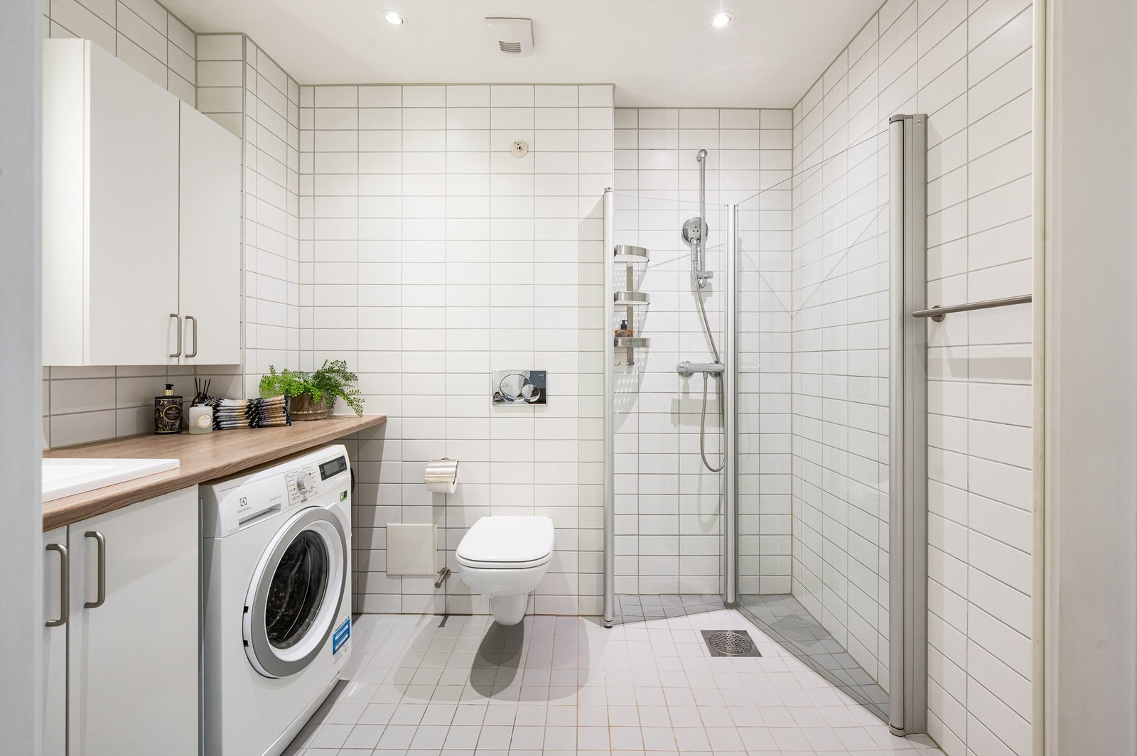 Lyst og delikat flislagt bad med gulvvarme og downlights. Badet består av benkeplate med servant, speil med belysning, vegghengt toalett og dusjhjørne med svingbare glassdører. Galleribilde