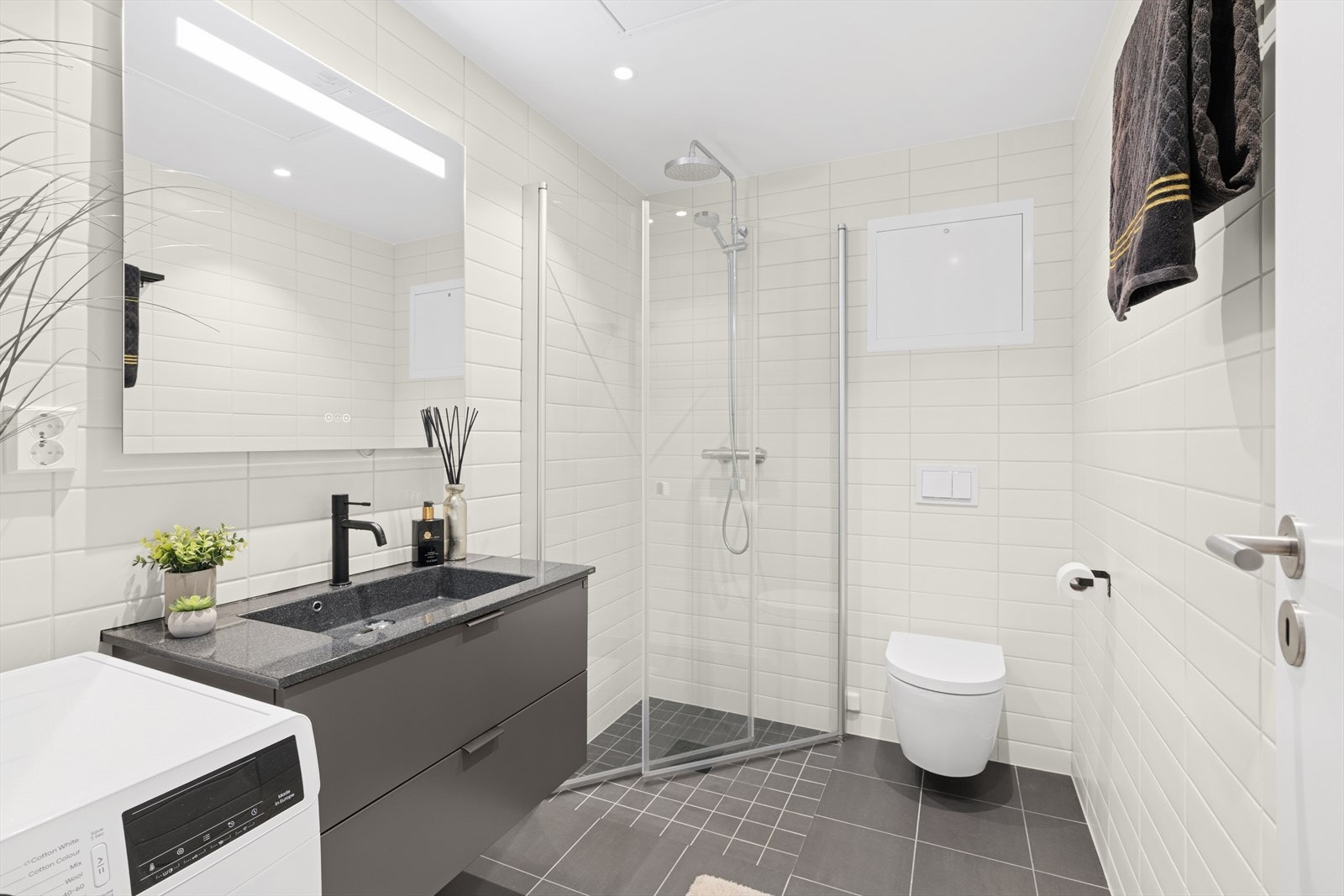 Badet er utstyrt med vegghengt wc, opplegg til vaskemaskin og tørketrommel, servant og dusjhjørne med glassvegger Galleribilde