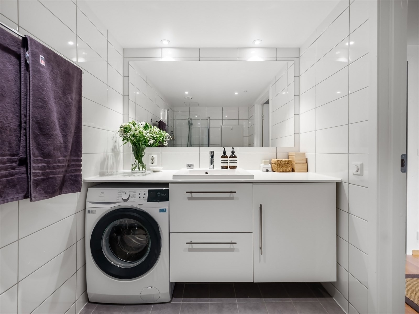 Badet har romslig servantinnredning med oppbevaringsplass og nisje for vaskemaskin, stort speil, dusj med glassdører og toalett. Galleribilde