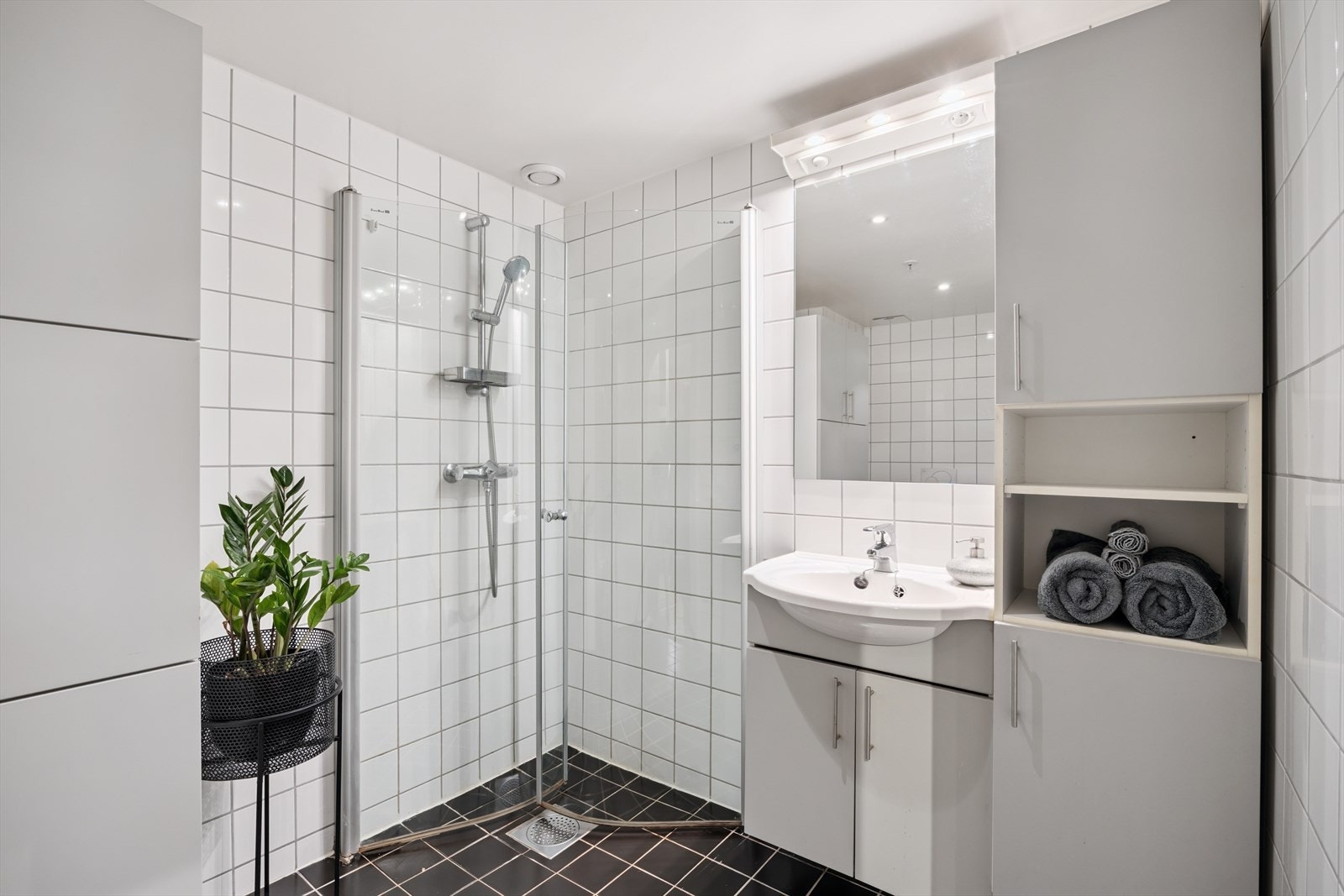 Delikat, flislagt bad med svingbare glassdører og moderne servantløsning. Galleribilde