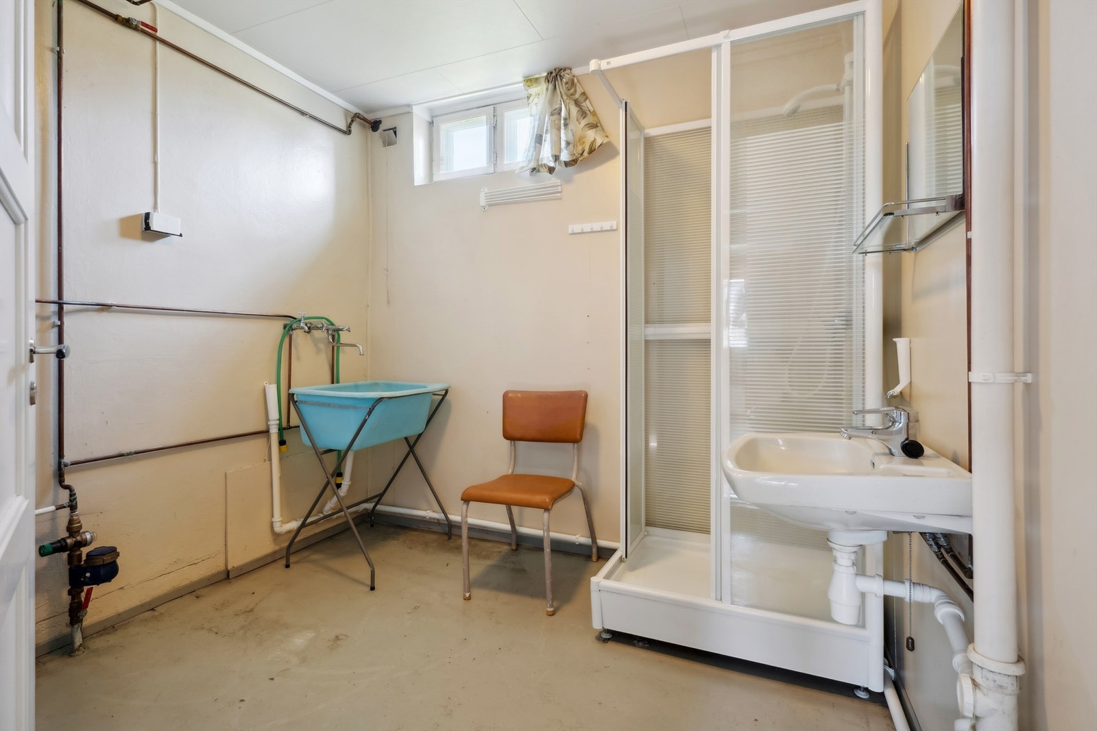 Eldre bad i underetasjen med dusjkabinett og opplegg for vaskemaskin. Behov for totalrenovering. Galleribilde