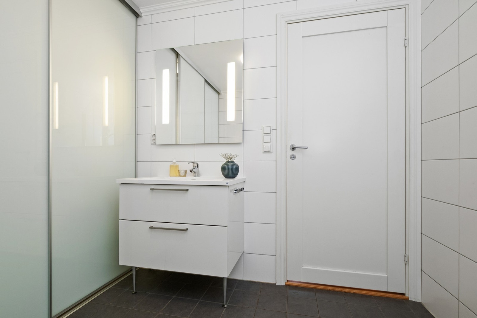 Baderomsinnredningen består av servant med hvite skuffer og et speil med lys integrert. Galleribilde