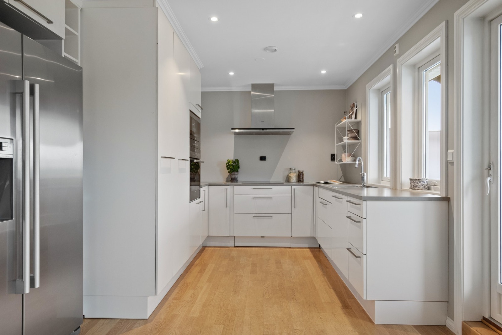 Ovnene er praktisk plassert i et høyskap, og over kokesonen har kjøkkenet en komfyrvakt og en ventilator med avtrekk ut. Downlights i taket tilfører ekstra lys til arbeidsflatene. Galleribilde