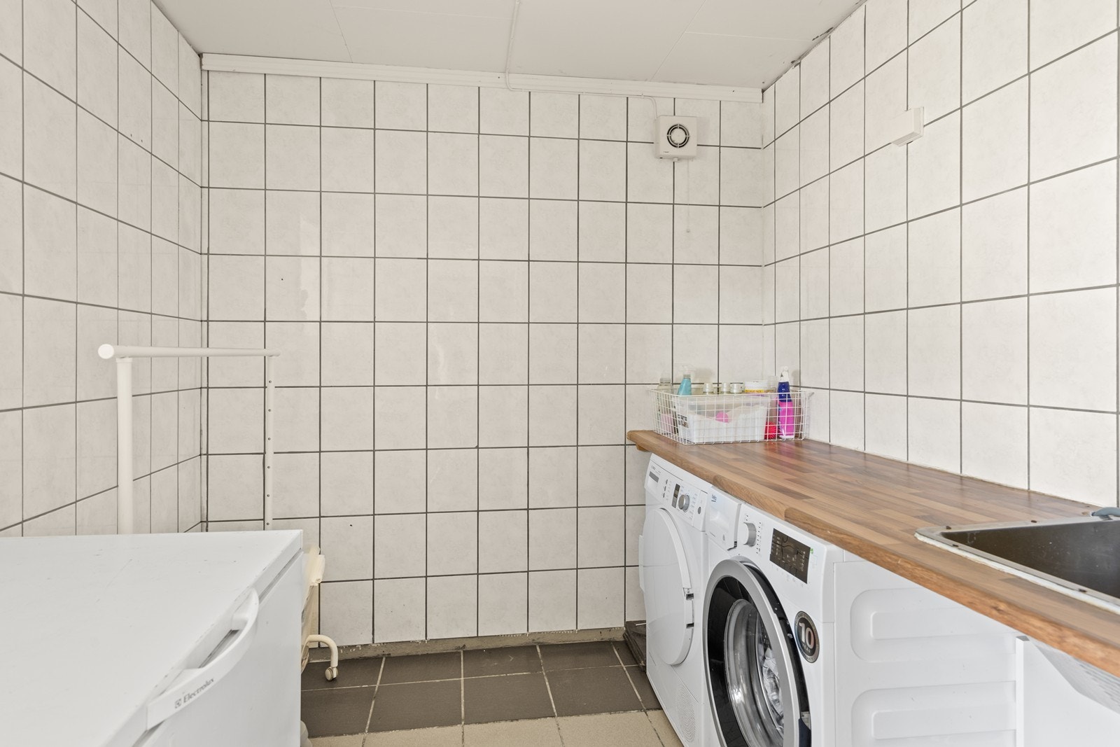 Et praktisk flislagt vaskerom med arbeidsbenk, nedfelt vaskekum og varmekabler i gulvet. Galleribilde