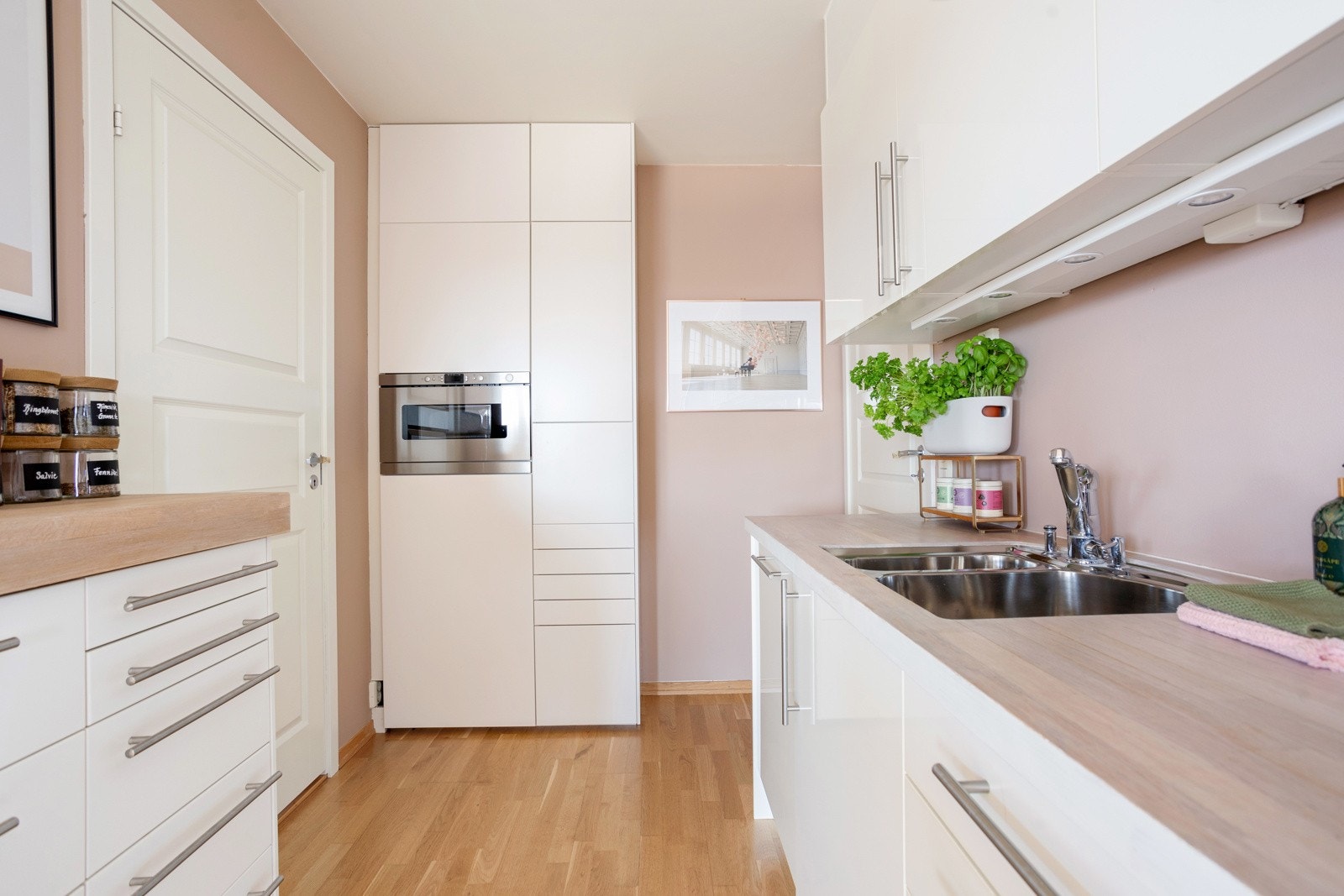 Stilren kjøkkeninnredning fra Norema med glatte fronter, belysning under overskap, heltre benkeplate med underlimt oppvaskkum og ventilator. Galleribilde
