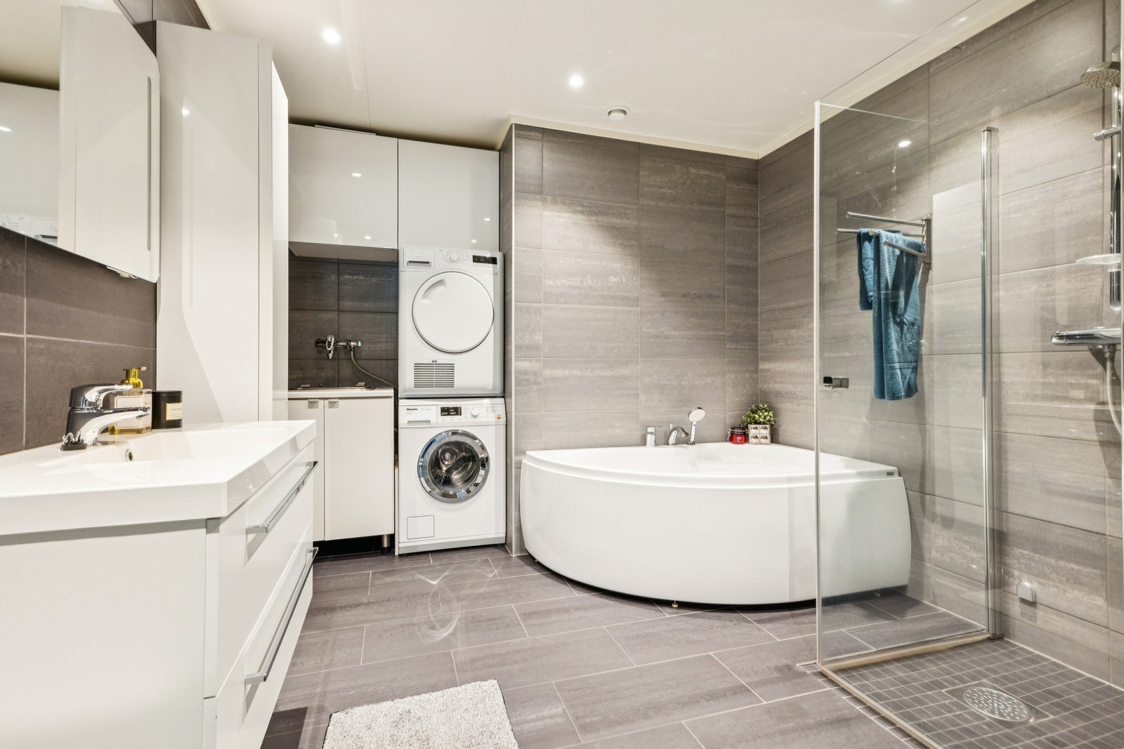 Romslig flislagt bad med egen sone for vaskemaskin, stort badekar og dusj. Galleribilde