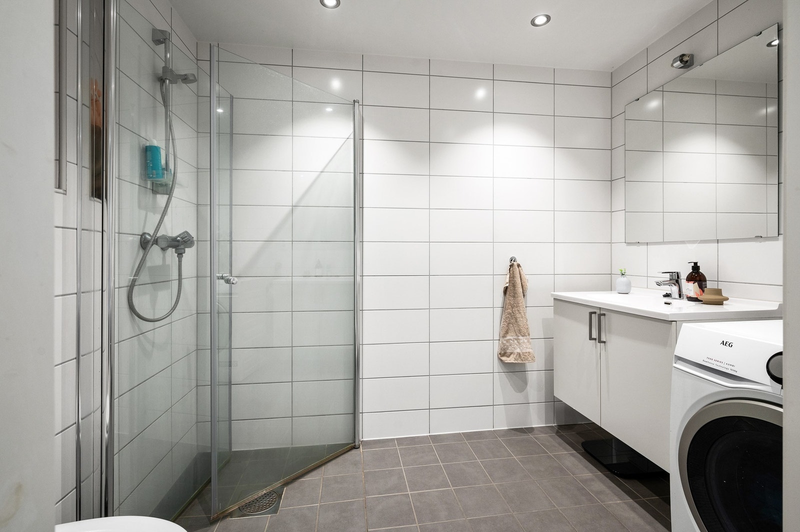 Leilighetens baderom med flislagt og det er vannbåren varme under gulvet. Spotter i tak, opplegg for vaskemaskin og innfellbare dusjdødrer Galleribilde