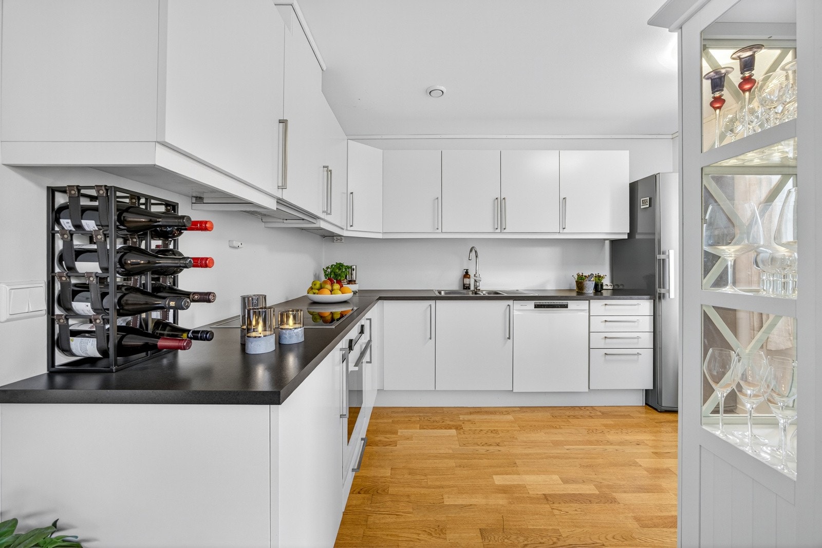 Moderne HTH-kjøkken i delvis åpen løsning mot stuen, fra byggeår. Kjøkkenet har rikelig med skap og benkeplass. Galleribilde