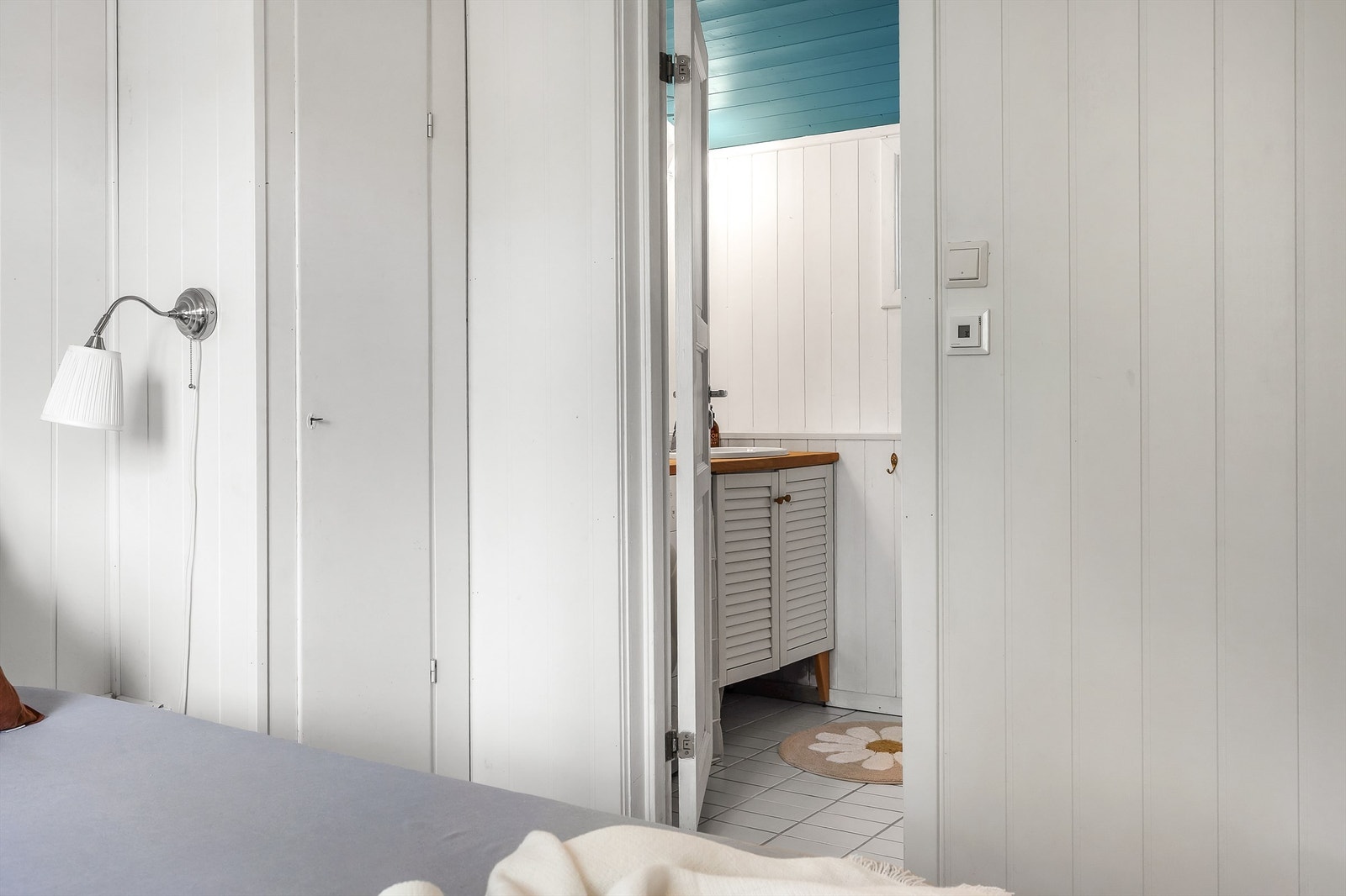 Baderom flislagt gulv med varme. Veggflater med fliser og malt panel. Skråtak med malt panel. Vegghengt servantskap med profilerte fronter. Benkeplate av heltre. Nedsenket servant med ett-greps armatur. Ikke godkjent for varig opphold. Galleribilde