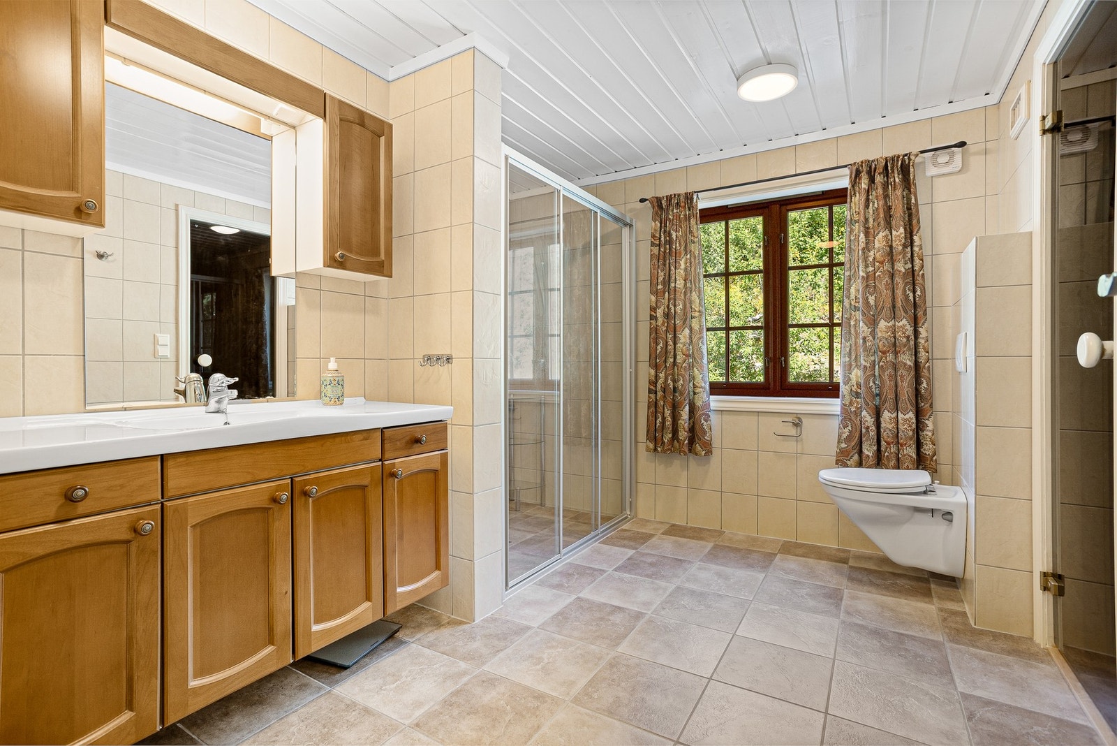 Romslig baderom med veggmontert toalett, innredning med servant og dusjnisje med glassdør Galleribilde