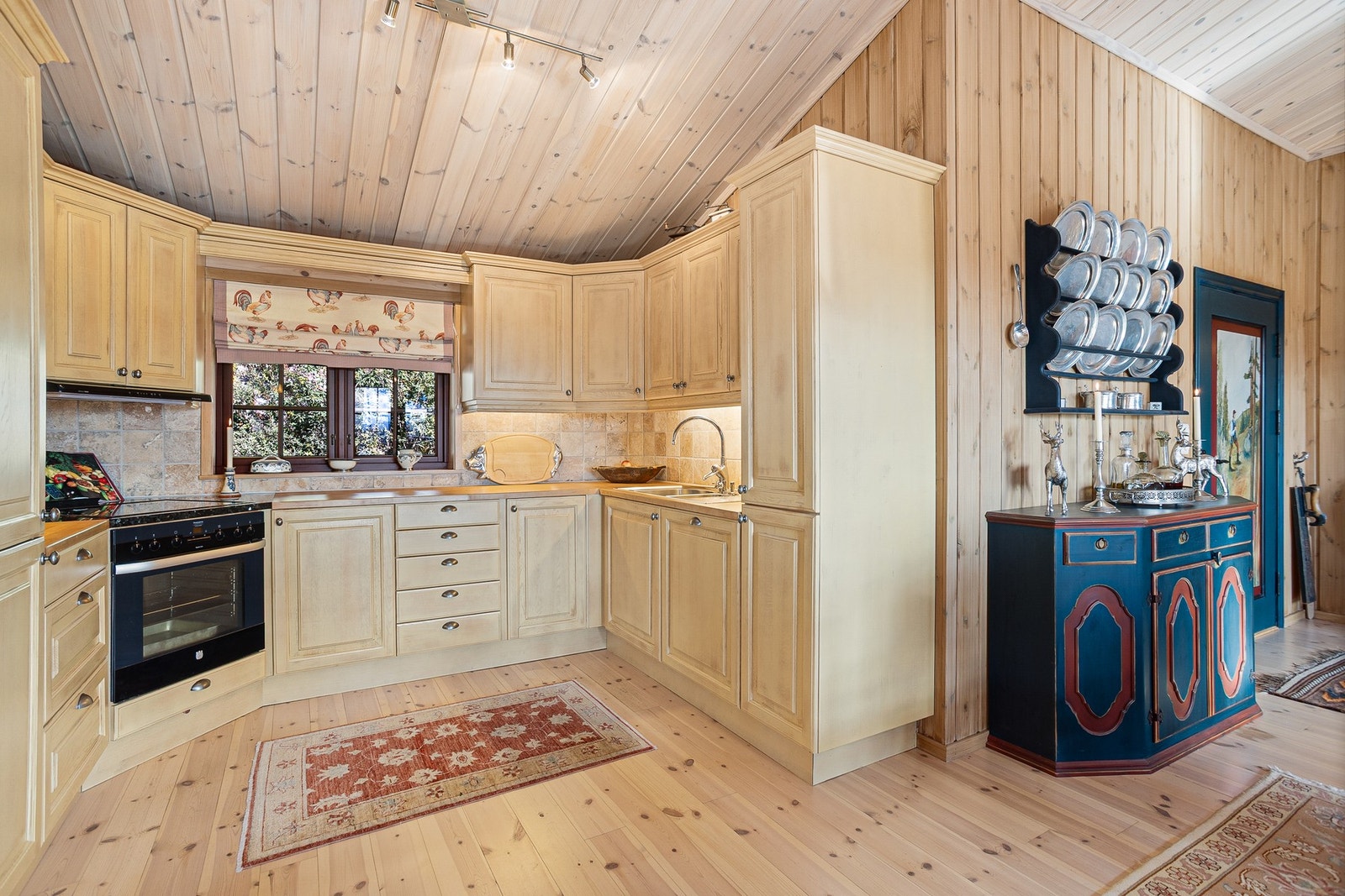 Kjøkken med innredning i lasert heltre. Profilerte fronter og benkeplate i heltre med steinplate rundt steketopp Galleribilde