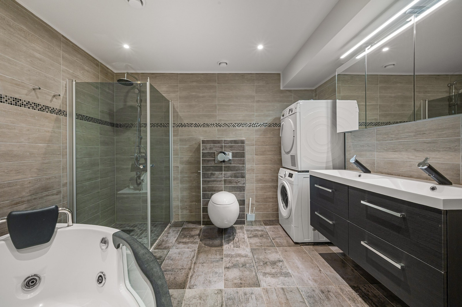 Moderne bad fra 2018 innredet med badekar, dusjhjørne, veggehengt toalett, dobbelservant og opplegg til vaskemaskin og tørketrommel. Galleribilde