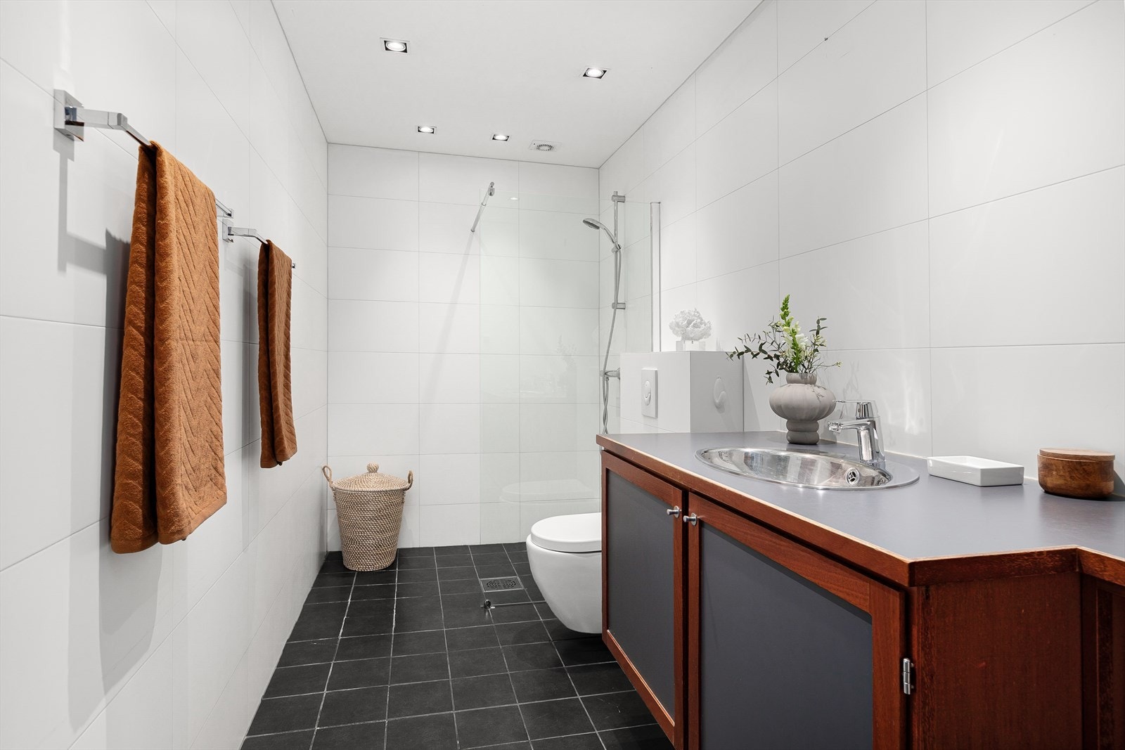 Baderommet er utstyrt med dusj på gulv med dør/felt i herdet glass, veggfestet klosett og servant med innredning Galleribilde