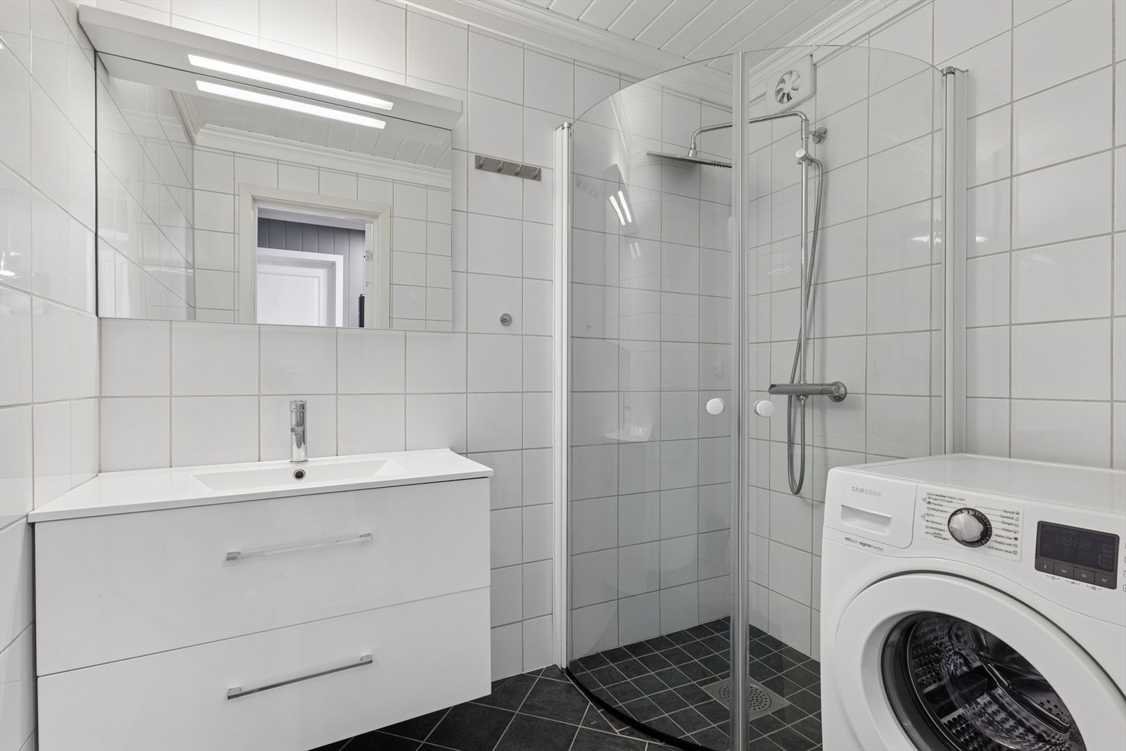 Flislagt bad fra 2015 med regnfallsdusj, servant med underskap, speil med belysning og opplegg for vaskemaskin. Galleribilde