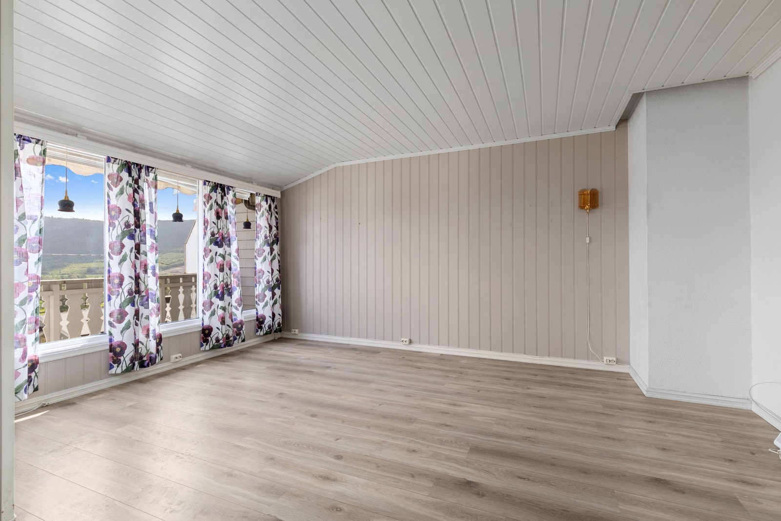 Leilighetens stue har store vindusflater som bidrar til å slippe inn rikelig med naturlig lys. Laminat på gulv, panelovn på vegg og utgang til balkong. Galleribilde