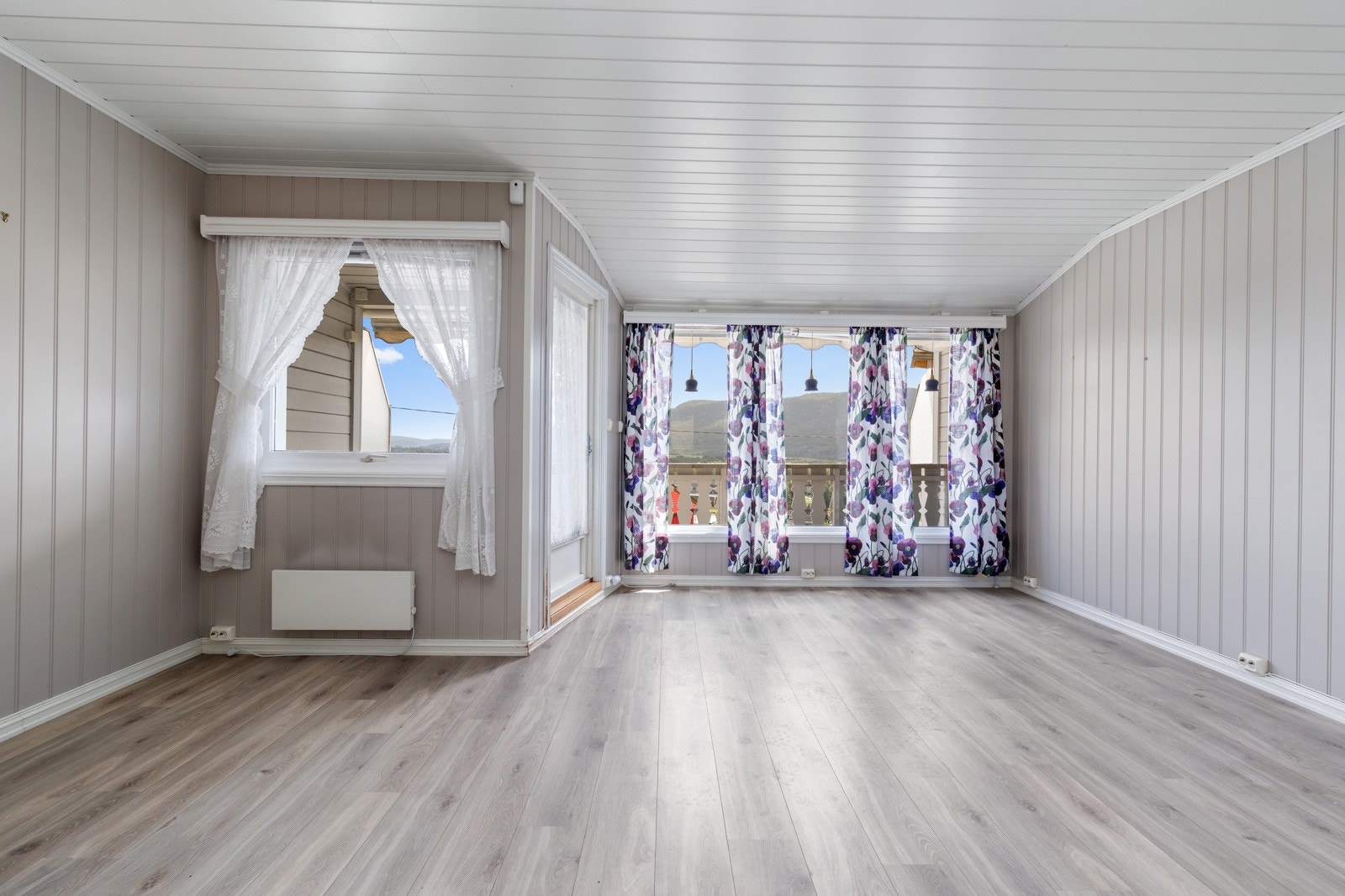 Leilighetens stue har store vindusflater som bidrar til å slippe inn rikelig med naturlig lys. Laminat på gulv, panelovn på vegg og utgang til balkong. Galleribilde