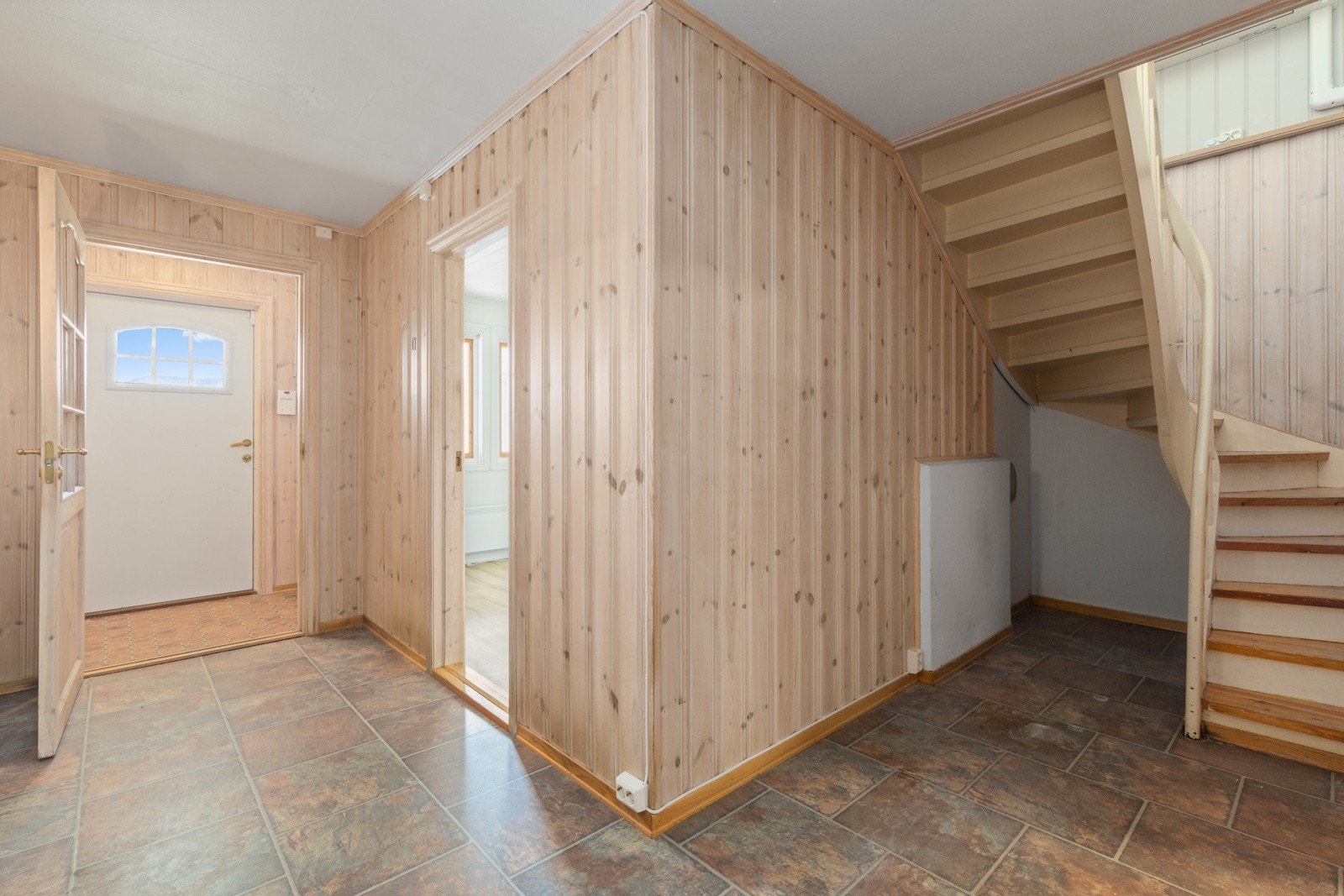 Entré og gang med fliser og gulvbelegg. Pipeløp til ildsted er til venstre for trappen. Ildsted er fjernet, men det er mulig å sette inn igjen. Varmepumpe montert over trapp. Galleribilde