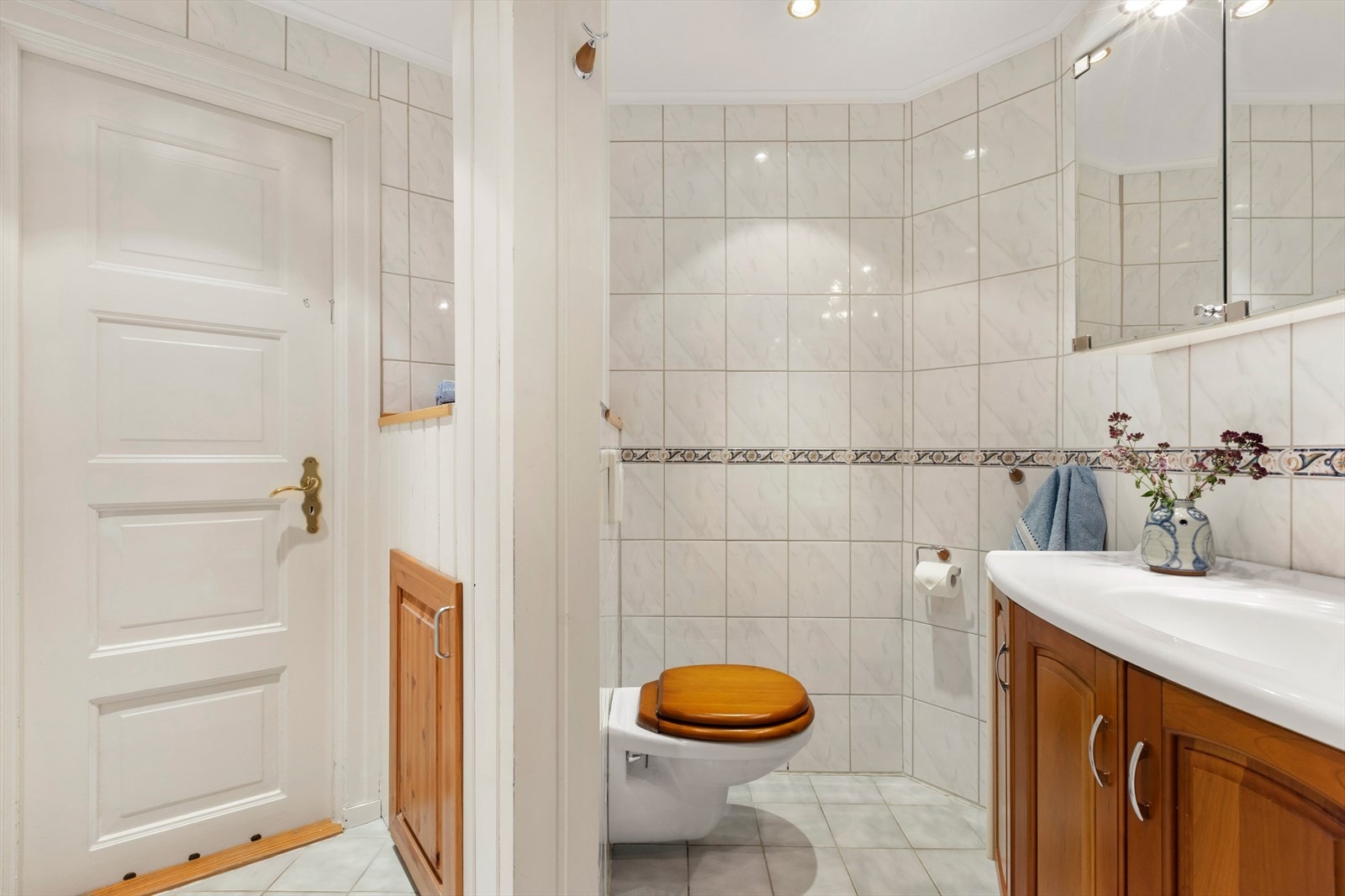 Romslig, flislagt bad fra 1997. Badet er innredet med vegghengt toalett, servant med underskap, speilskap med lys, og en stor dusjsone med glassvegger. Galleribilde